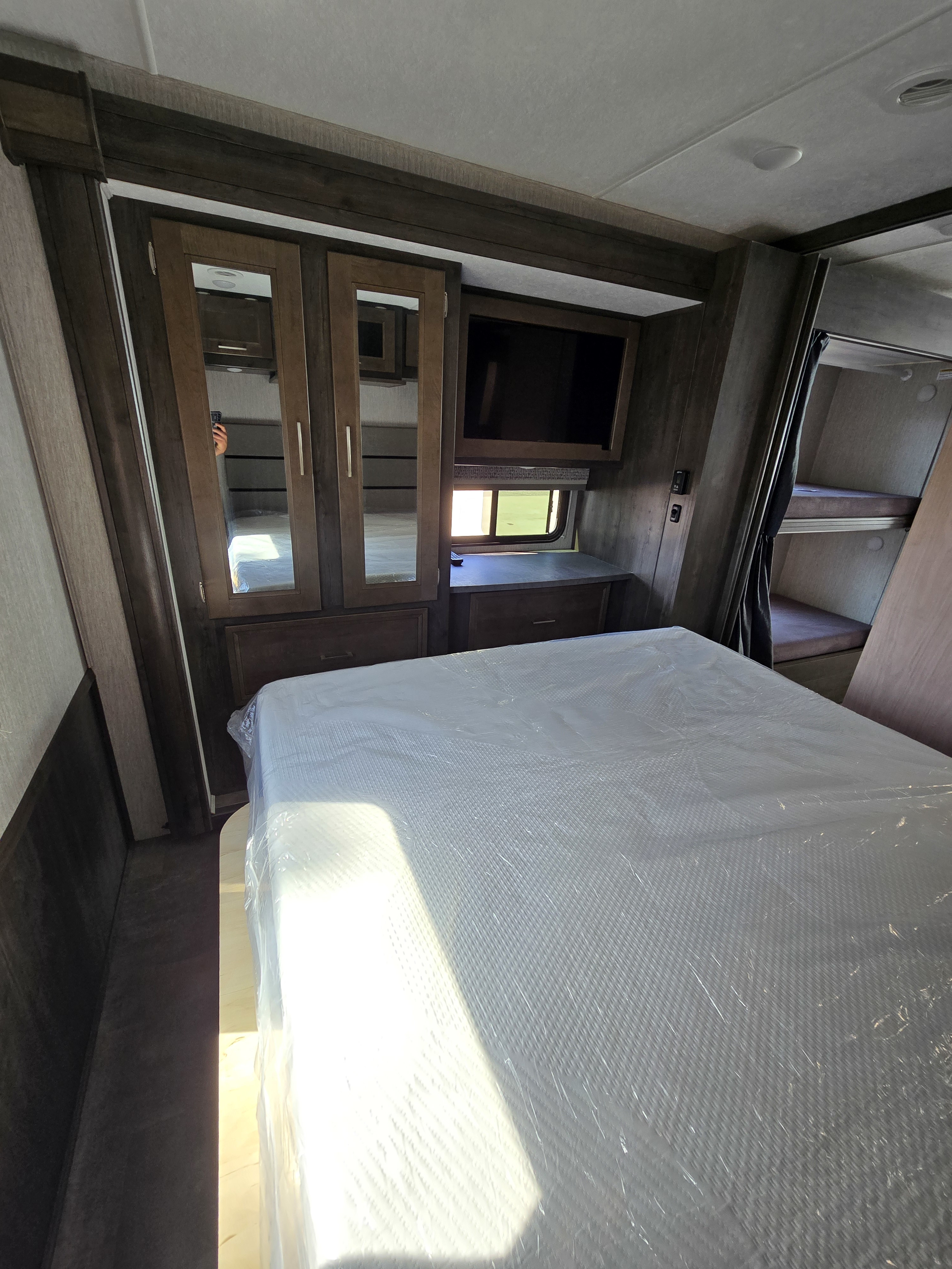 Interior view of an RV bedroom with a new bed, mirrored wardrobe, TV, and bunk beds, ideal for your next RV rental.. Forest River Coachmen Pursuit 2021