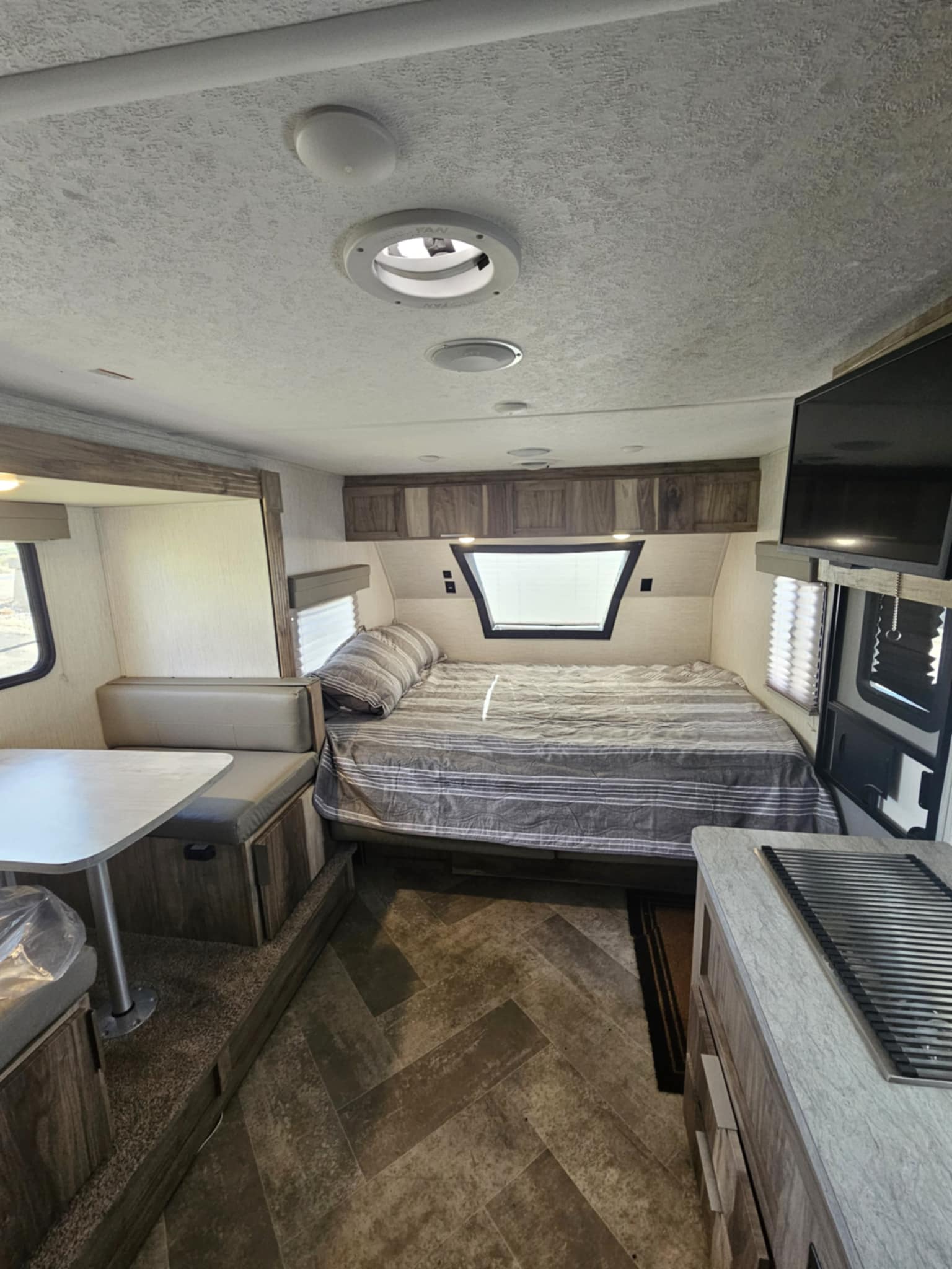 RV rental interior: cozy bed with striped bedding, dinette, kitchen counter with stovetop, and mounted TV.. Palomino 189BHS 2022