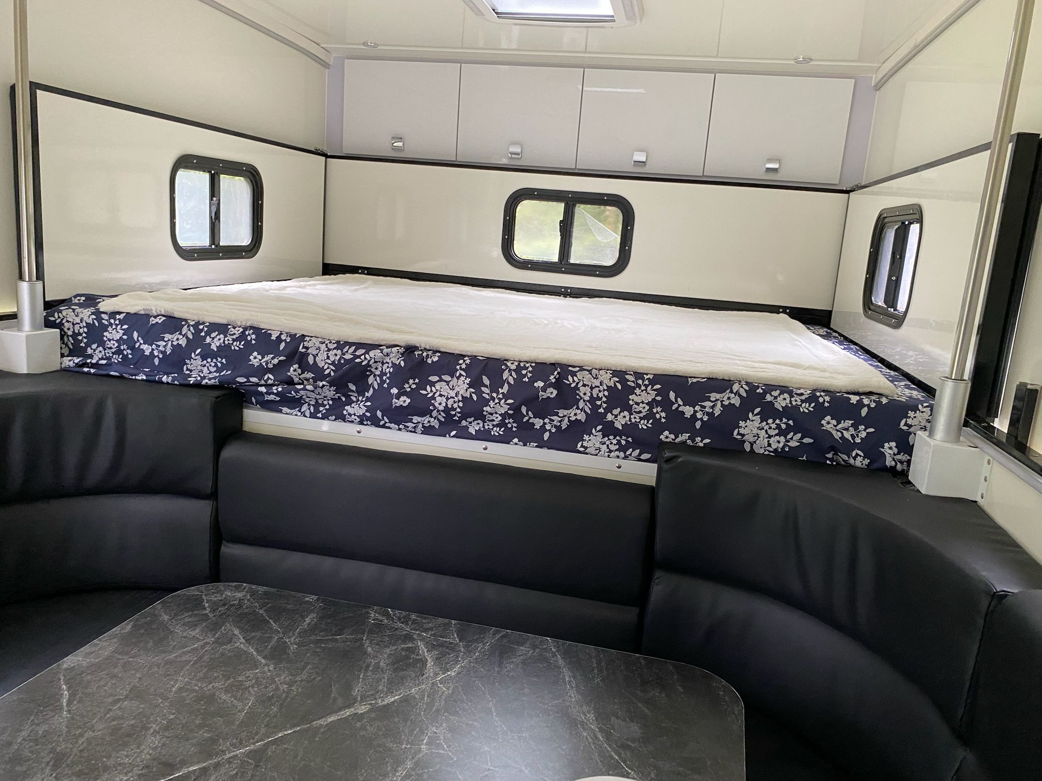 Spacious RV rental interior. Features a large bed with floral bedding, U-shaped black seating, and a dining table.. Desert Overlander Ibex 2022