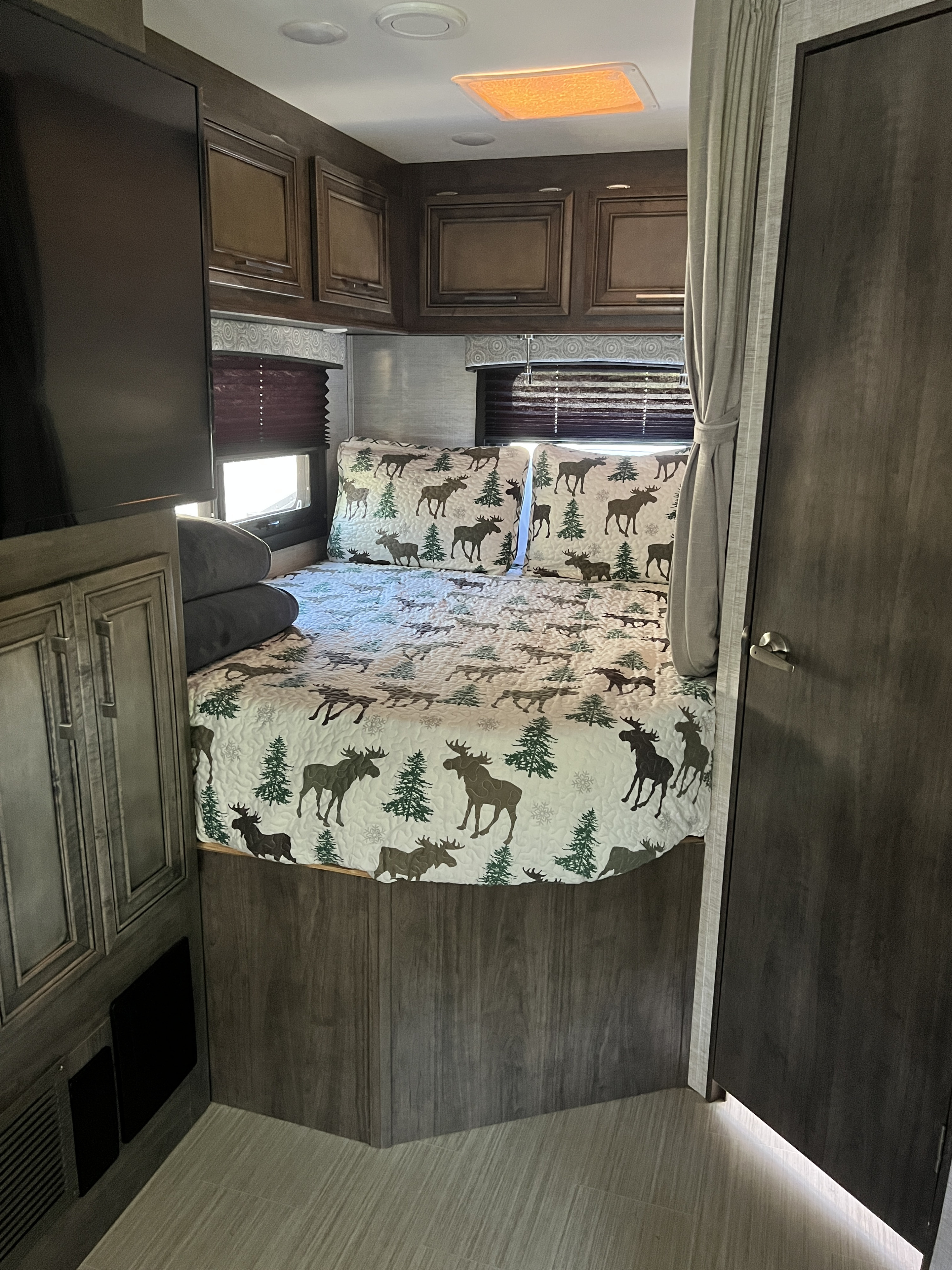 Cozy RV rental bedroom featuring moose bedding, a TV, and overhead storage. Perfect for a comfortable escape!. Entegra Coach Odyssey 2022
