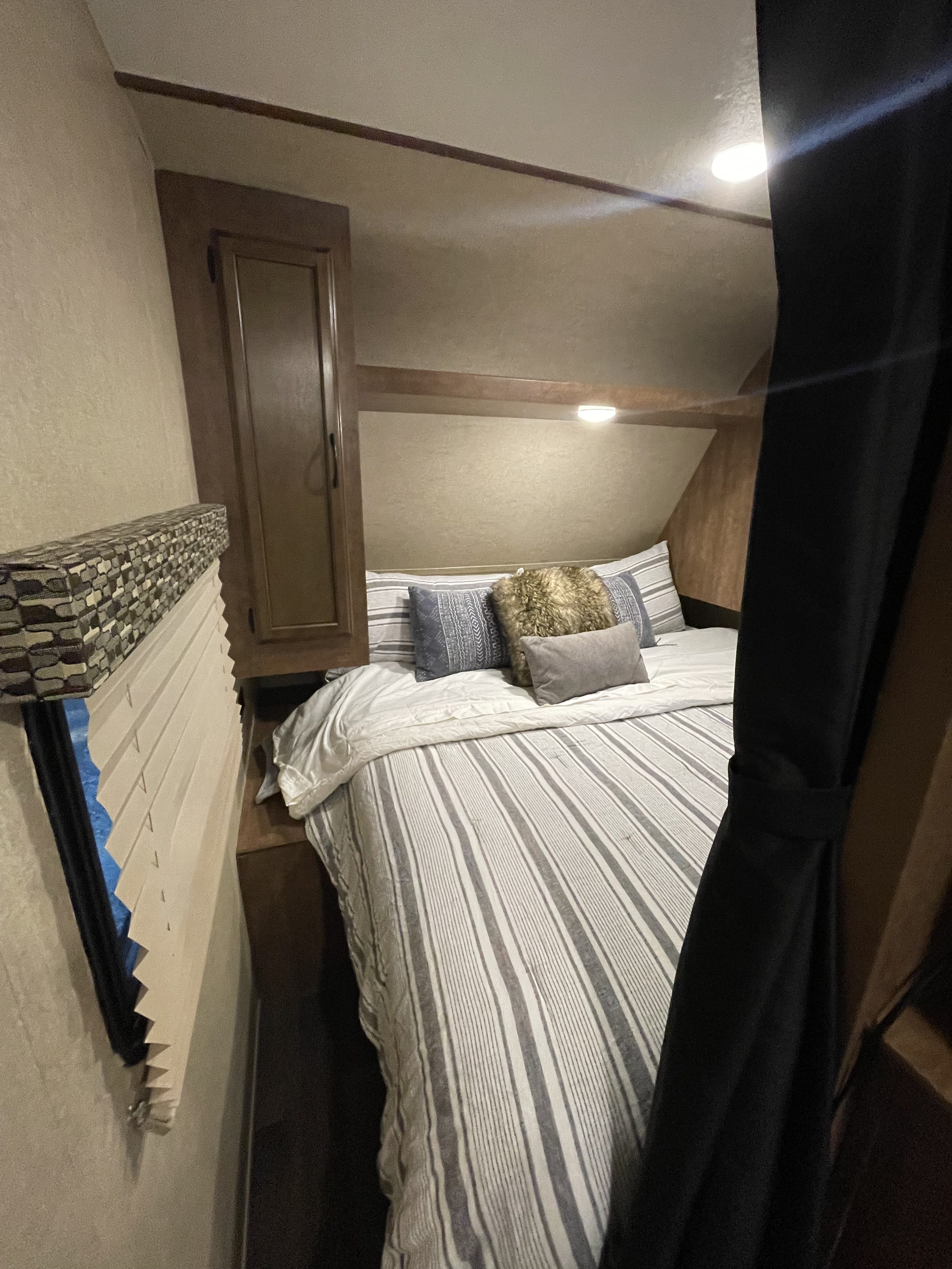 Cozy RV rental bedroom with striped bedding, storage cabinet, and window blinds, offering comfortable travel lodging.. Starcraft Autumn Ridge Outfitter 2018