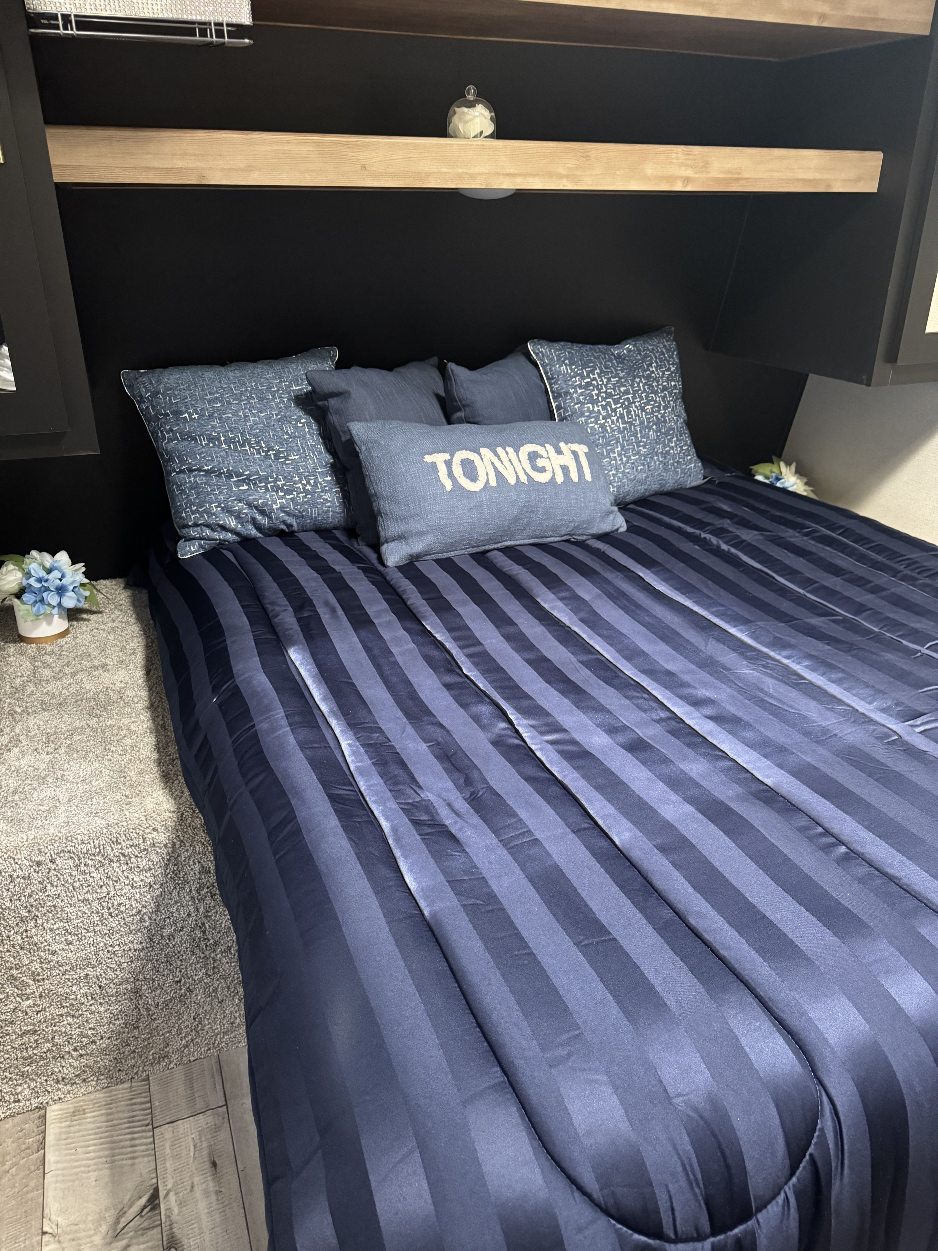 Explore this cozy RV rental bedroom. It features blue striped bedding, a "TONIGHT" pillow, and a compact, well-designed space.. Keystone RV Springdale 2022