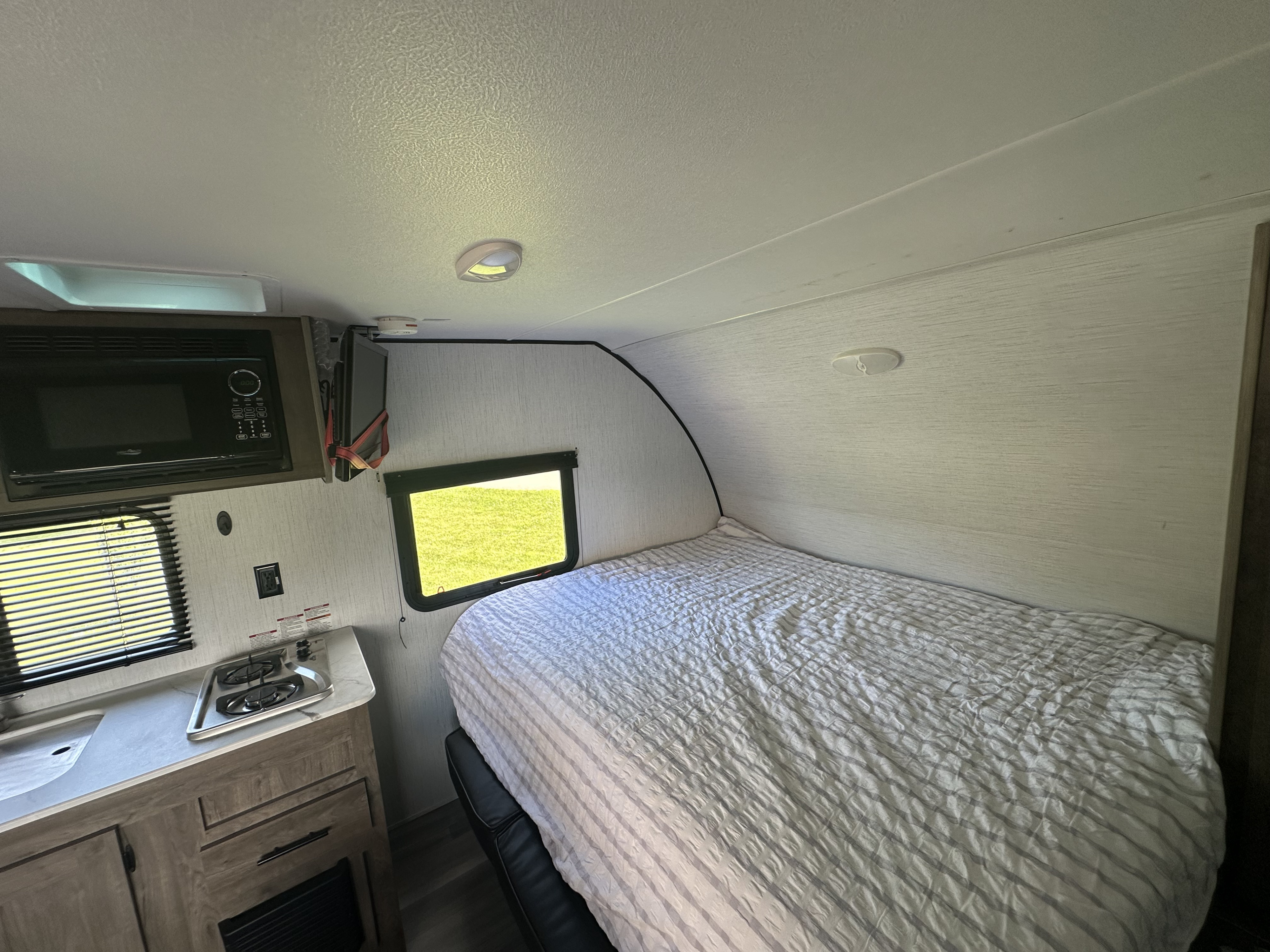 Bright rv rental interior showing a compact kitchen with microwave & stove, plus a cozy bed area with a window.. Heartland RVs Pioneer Trail Blazer 2022