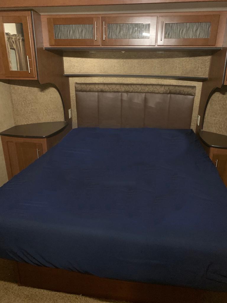 Cozy RV rental bedroom featuring a large bed with blue sheets, brown headboard, and built-in wood cabinets for comfort.. Dutchmen Komfort 3130 FRL 2011