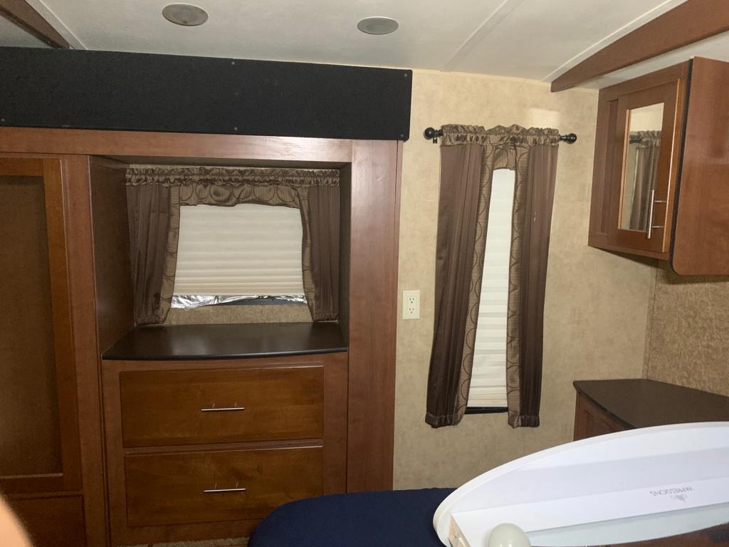 Cozy RV rental bedroom showcases wooden cabinetry, windows with blinds and brown curtains, an overhead mirrored cabinet, and a bed.. Dutchmen Komfort 3130 FRL 2011