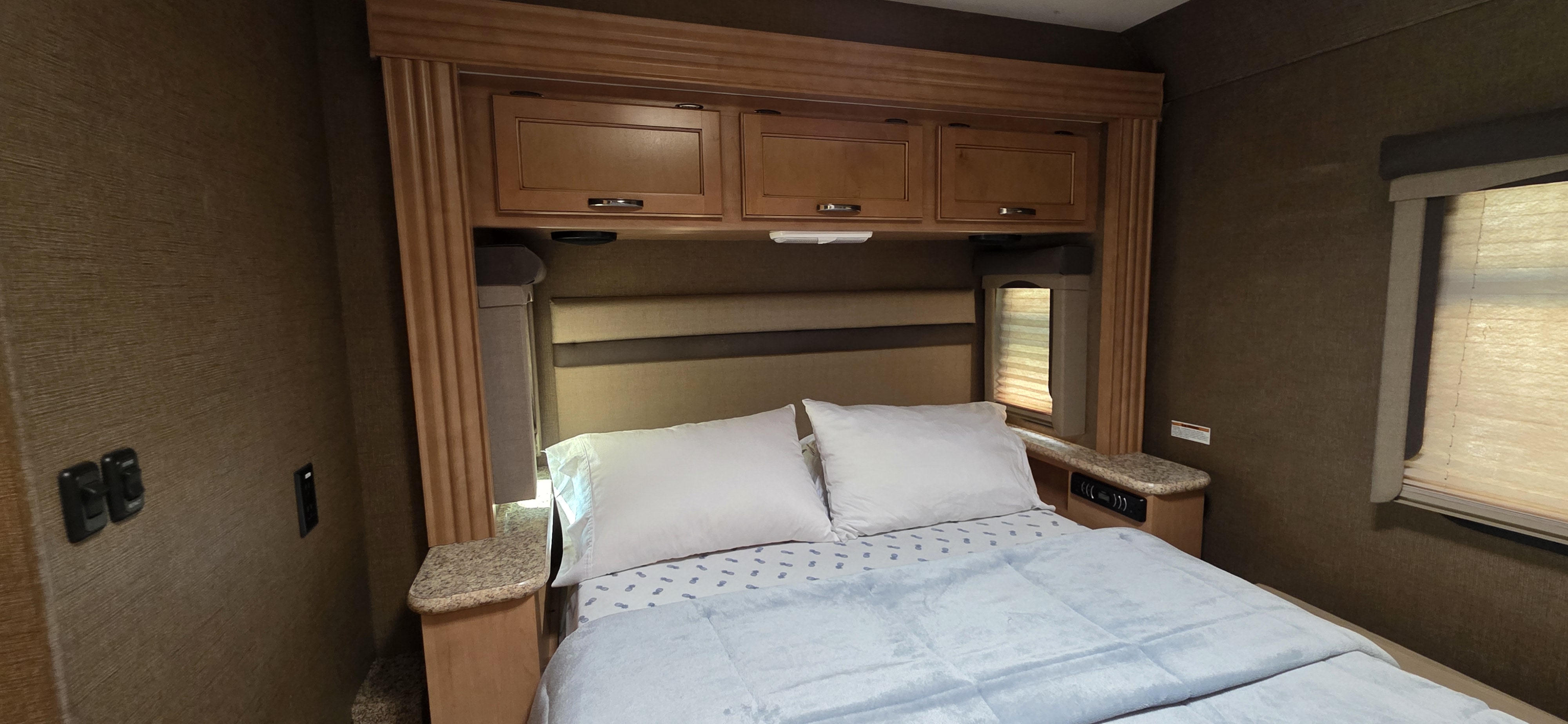 View of a compact RV rental bedroom with a comfy bed, white pillows, and blue bedding. Includes overhead cabinets and bedside tables.. A.C.E. A.C.E. Motorhome 2015