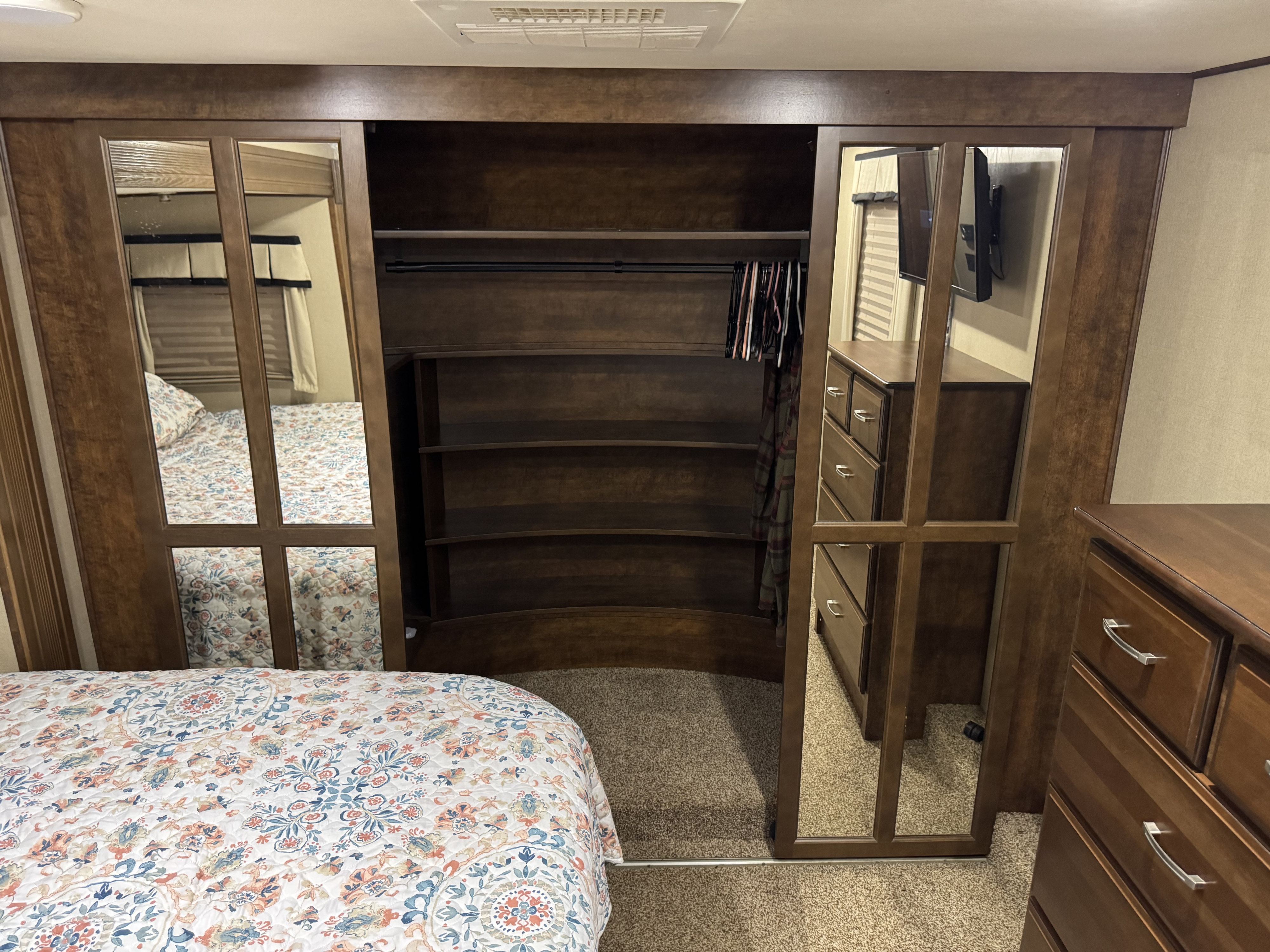 RV rental bedroom: Mirrored wardrobe, built-in shelves, dresser, and cozy patterned bed for comfortable living.. Grand Design Momentum Toy Hauler 2014