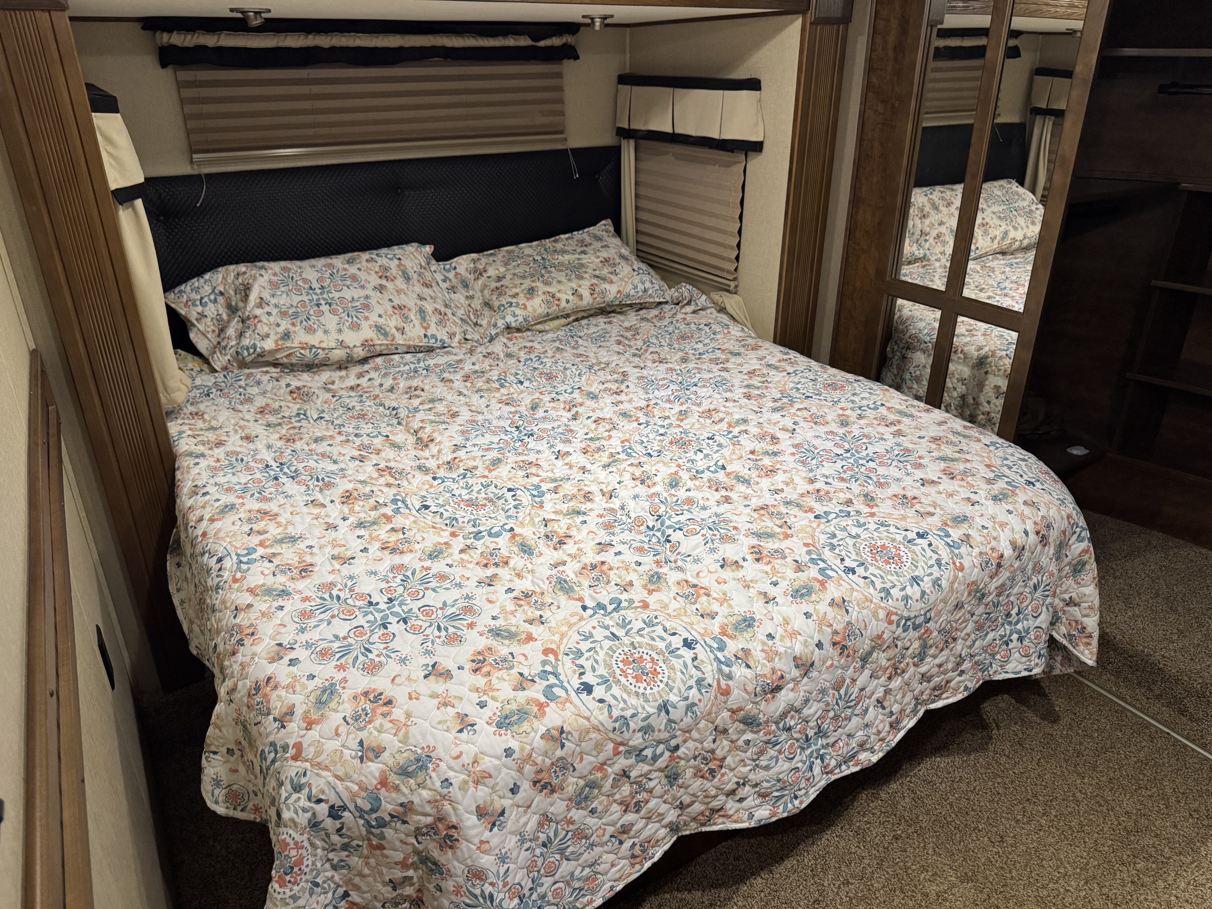 Cozy RV rental bedroom with floral quilt, black headboard, window blinds, and built-in storage. Ideal for travel comfort.. Grand Design Momentum Toy Hauler 2014