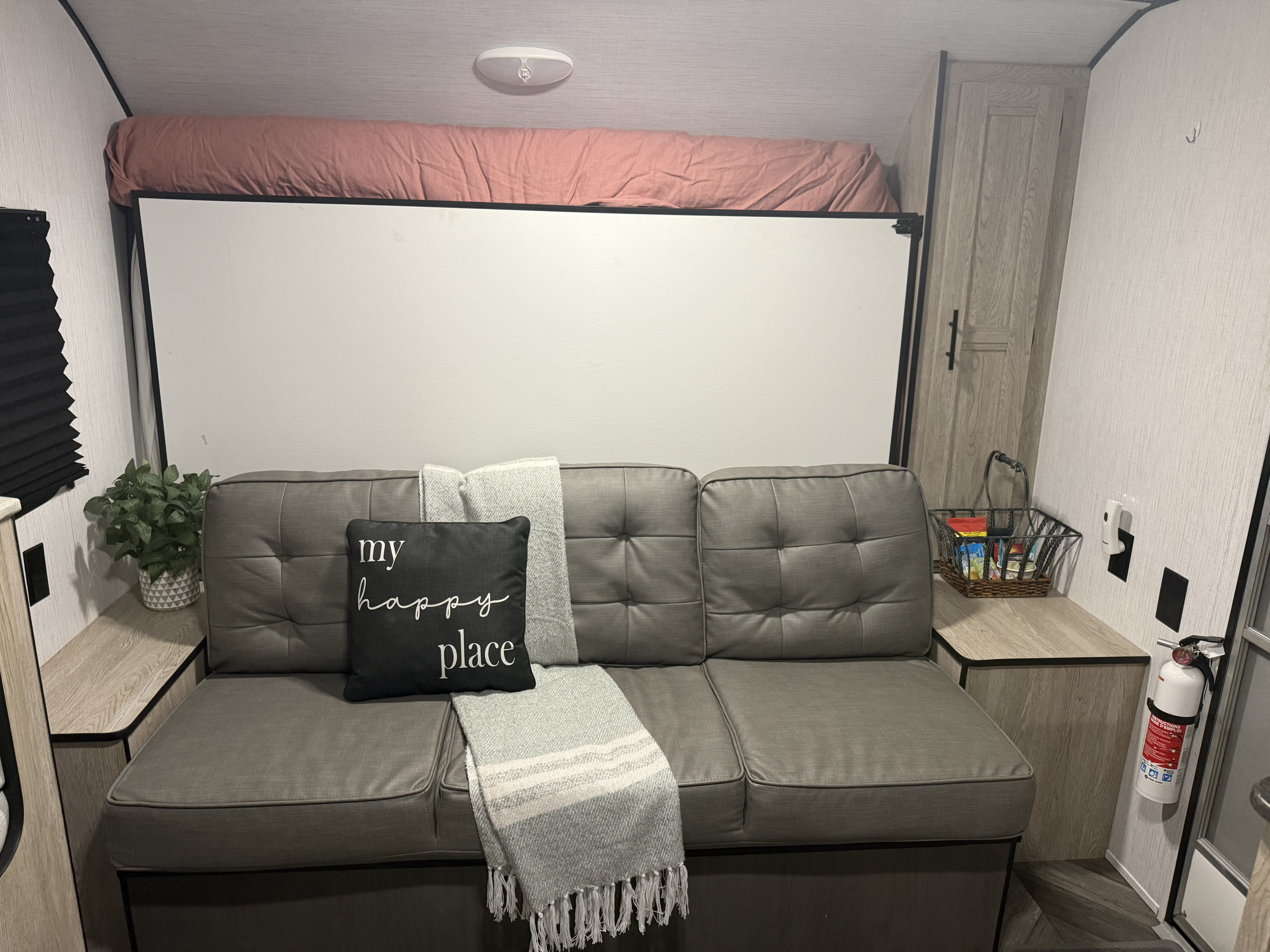 Inside a modern RV rental, featuring a gray sofa, fold-down bed, decor, and safety essentials like a fire extinguisher.. Heartland RVs Prowler Lynx 2022