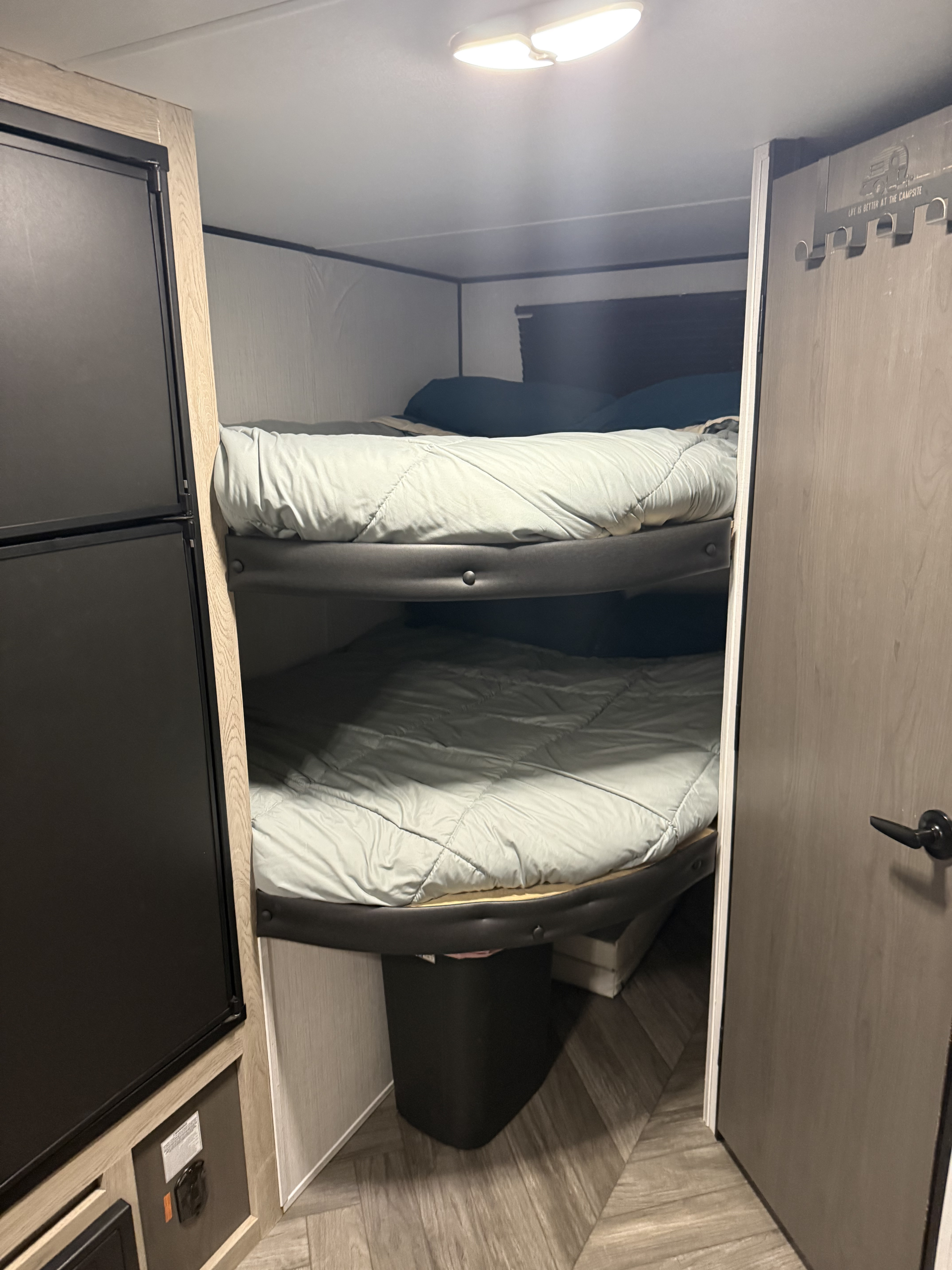 Cozy RV rental interior with bunk beds, refrigerator, and wood-paneled door. Ideal for camping trips.. Heartland RVs Prowler Lynx 2022