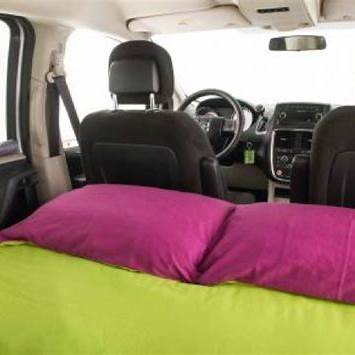 Minivan interior shows a green bed with pink pillows, ideal for car camping. A comfy RV rental alternative for road trips.. Dodge Caravan 2013