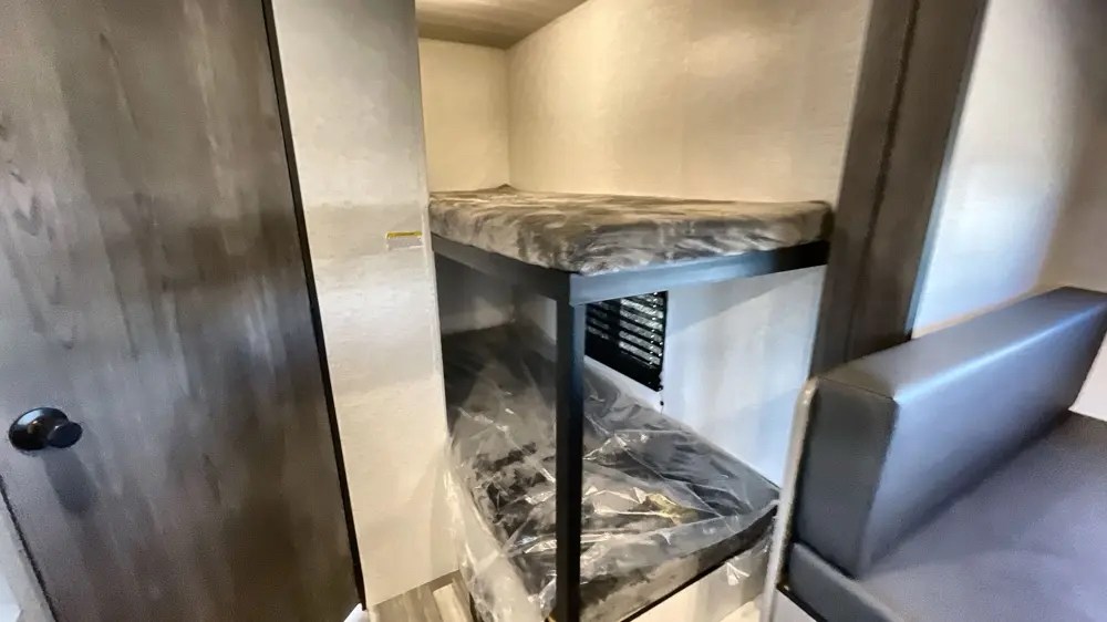 Explore this RV rental's interior: bunk beds (bottom still wrapped), wood-grain door, and seating.. Keystone RV Hideout Sport 2024