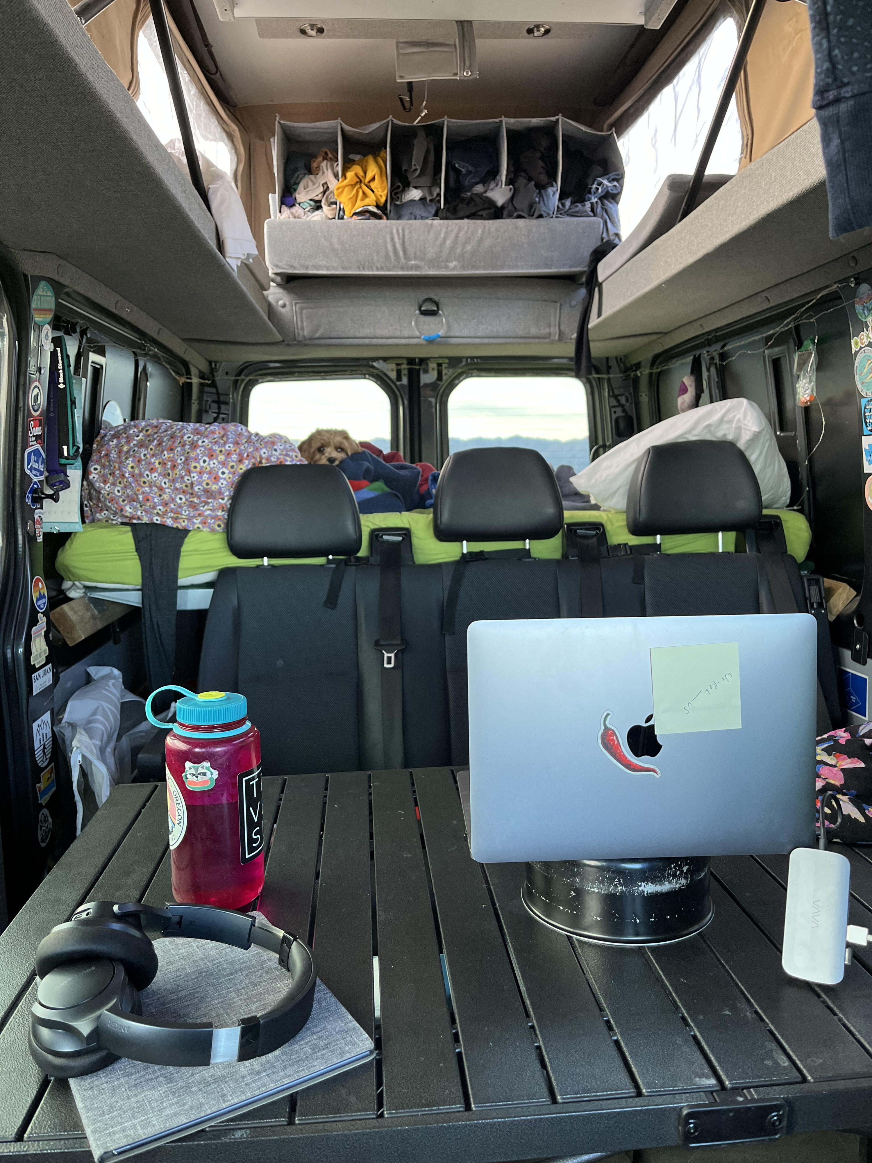 Cozy RV rental interior: A dog rests on the bed, while a mobile office setup with a laptop and headphones provides workspace.. Mercedes-Benz Sprinter 2015