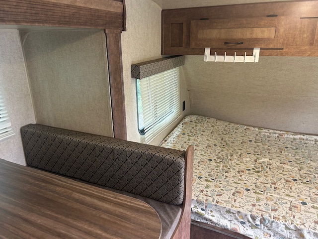 RV rental interior: A comfy bed with a light patterned blanket, dinette seating with a brown patterned cushion, wooden table & cabinets.. Starcraft Autumn Ridge Mini 2017