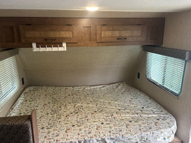 Cozy RV rental bedroom with a nature-themed bedspread, overhead cabinets, and windows with blinds. Perfect for your next adventure!. Starcraft Autumn Ridge Mini 2017