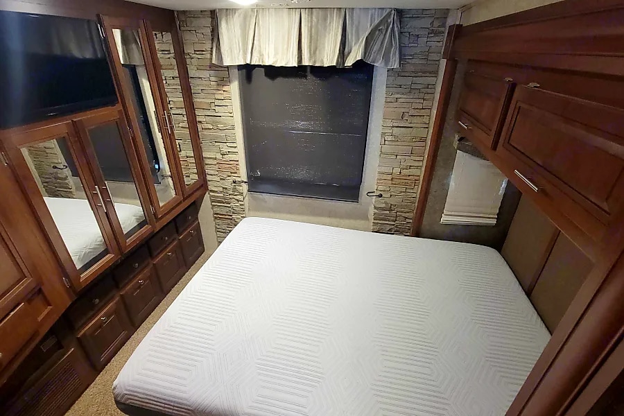 Experience comfort in this RV rental bedroom: plush bed, ample wooden storage, and TV. Stone accent wall.. Georgetown XL 2015