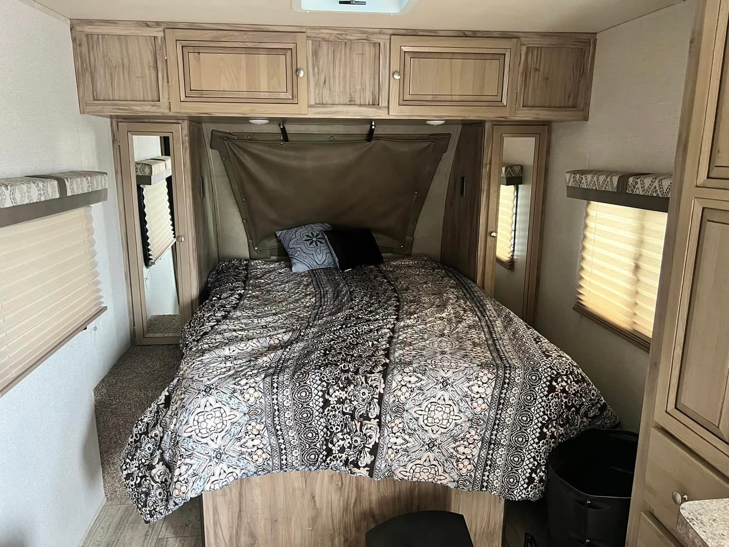 Cozy RV rental bedroom featuring a bed with patterned comforter, overhead cabinets, and compact wardrobe space.. Palomino Real Lite 2019