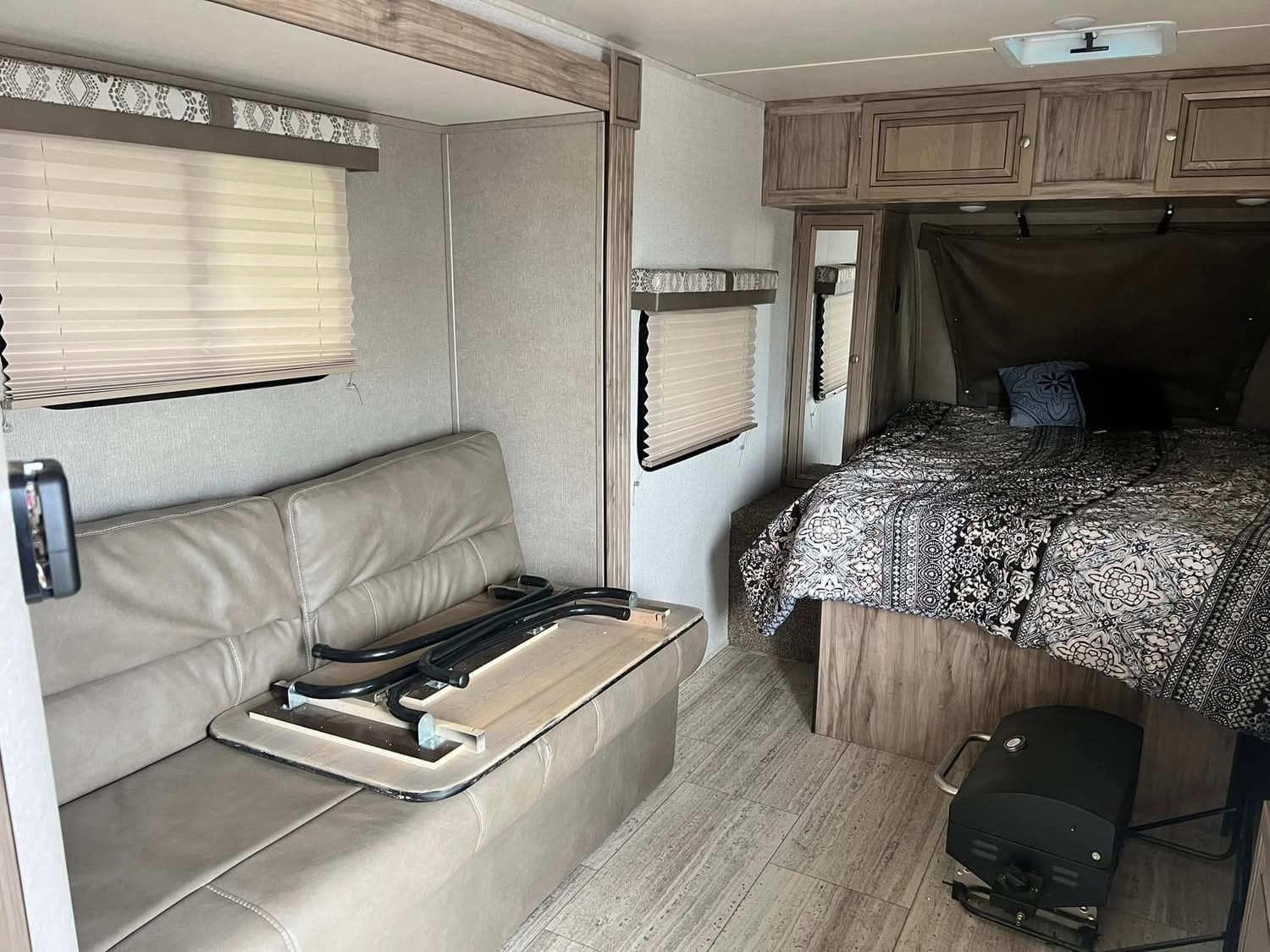RV rental interior features a comfortable bed with patterned bedding, a convertible sofa, and overhead cabinets. A portable grill sits on the floor.. Palomino Real Lite 2019
