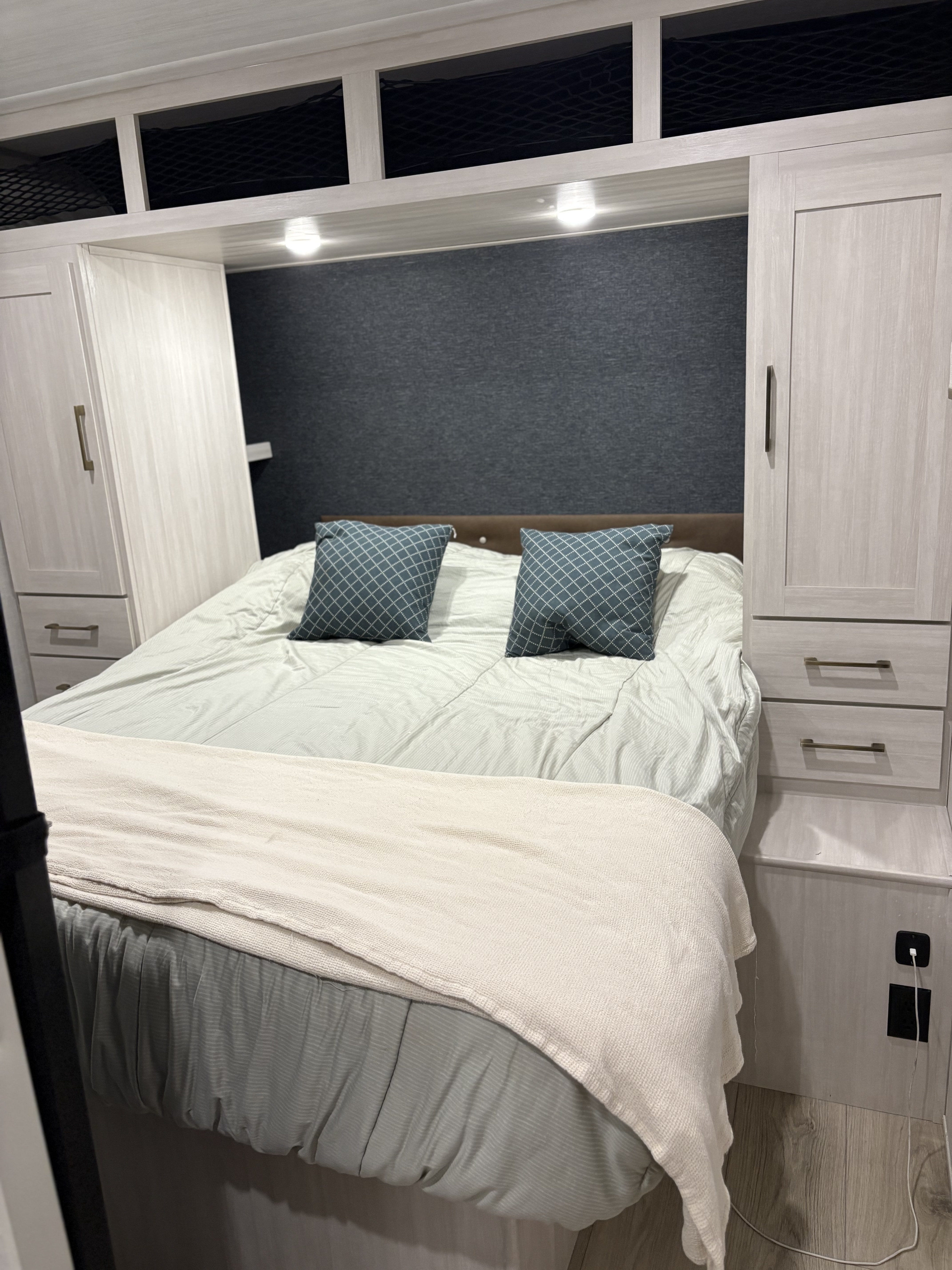 RV rental bedroom: Cozy bed, ample light wood built-in storage, overhead netting, and convenient charging.. Surveyor Legend X 27CAMP 2025