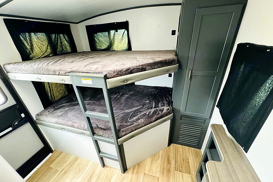 Cozy RV camper rental interior: double bunk beds, a ladder, wardrobe, and desk. Ready for your travels!. Keystone RV Bullet Ultra Lite 2022