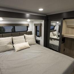 Experience RV rental comfort! This spacious RV bedroom features a large bed, striped pillows, windows, and a mirrored wardrobe for ample space.. Alliance RV Valor 2022