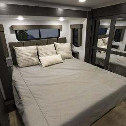 Modern RV rental bedroom featuring a large bed, windows, and mirrored closet. Ideal for travel comfort.. Alliance RV Valor 2022