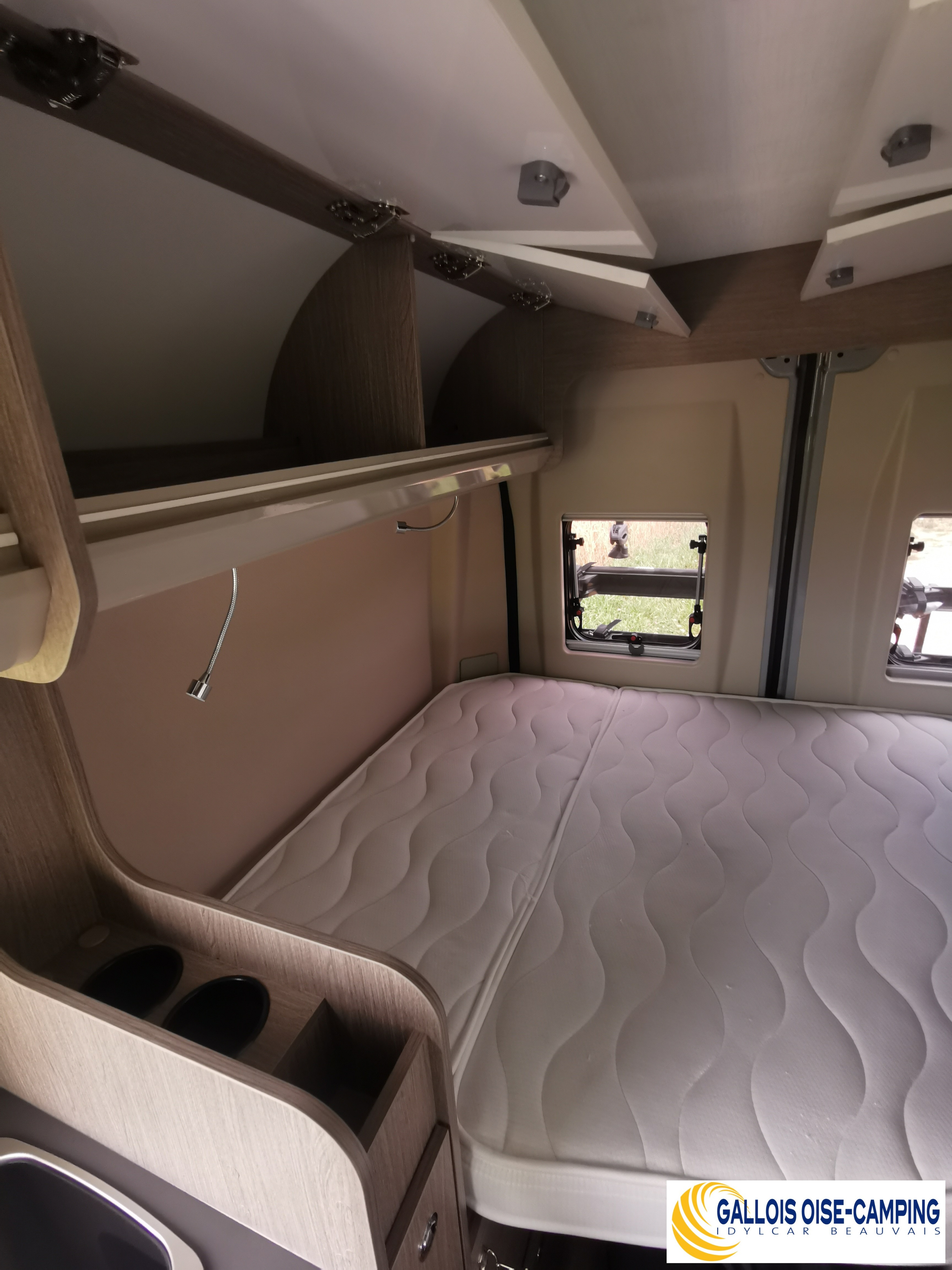 Inside a comfortable rv rental bedroom featuring a wavy mattress, overhead storage, and a reading lamp. Ready for travel!. challenger v114s 2023