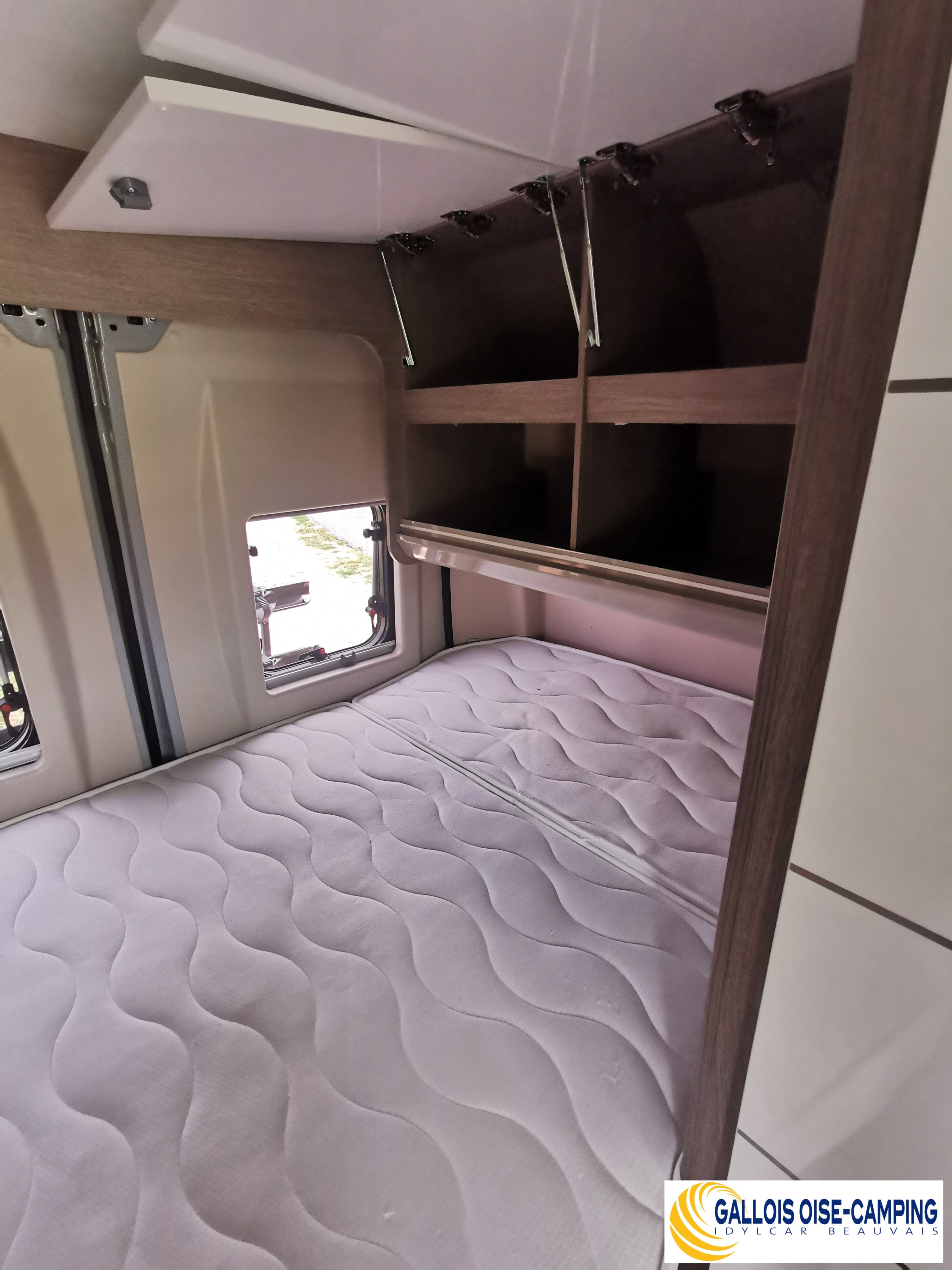 Inside this RV rental, find a cozy sleeping area featuring a wavy-patterned mattress and open overhead storage compartments.. challenger v114s 2023
