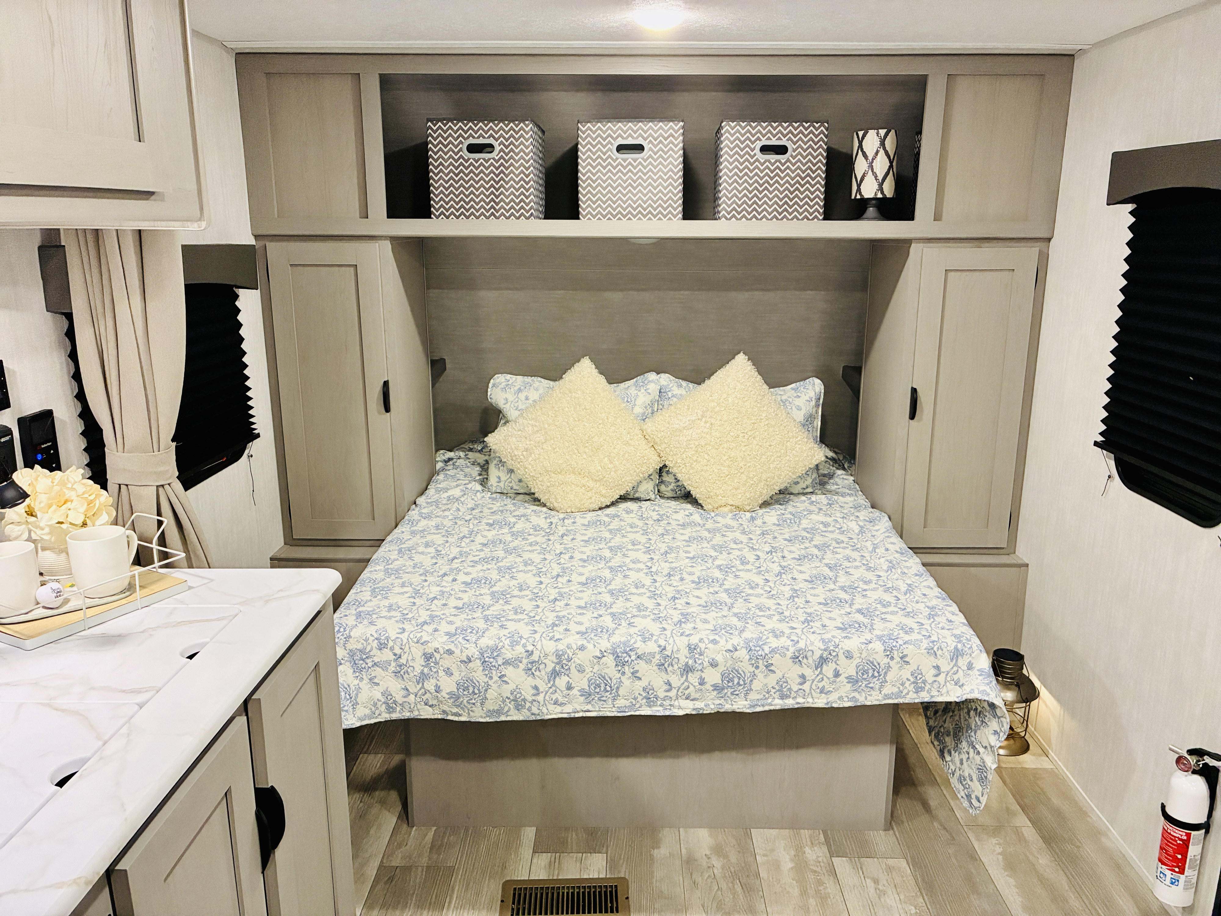 Bright RV rental bedroom: cozy bed with floral quilt, ample built-in storage, and light wood flooring.. Coachmen 25QBH 2025