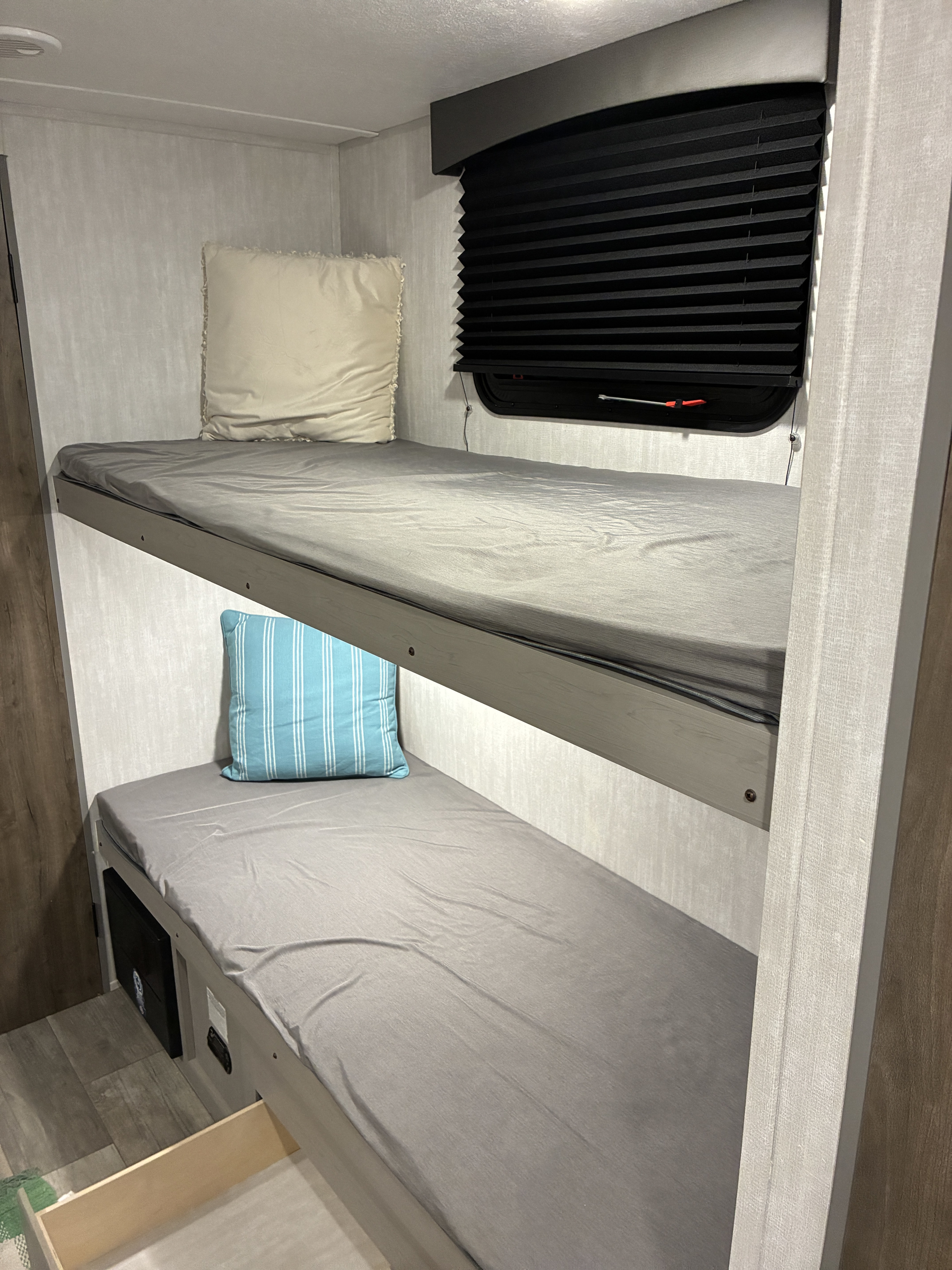 RV rental: Compact sleeping area with two bunk beds, fitted with grey sheets and pillows. Features window and under-bed storage.. Coachmen 25QBH 2025