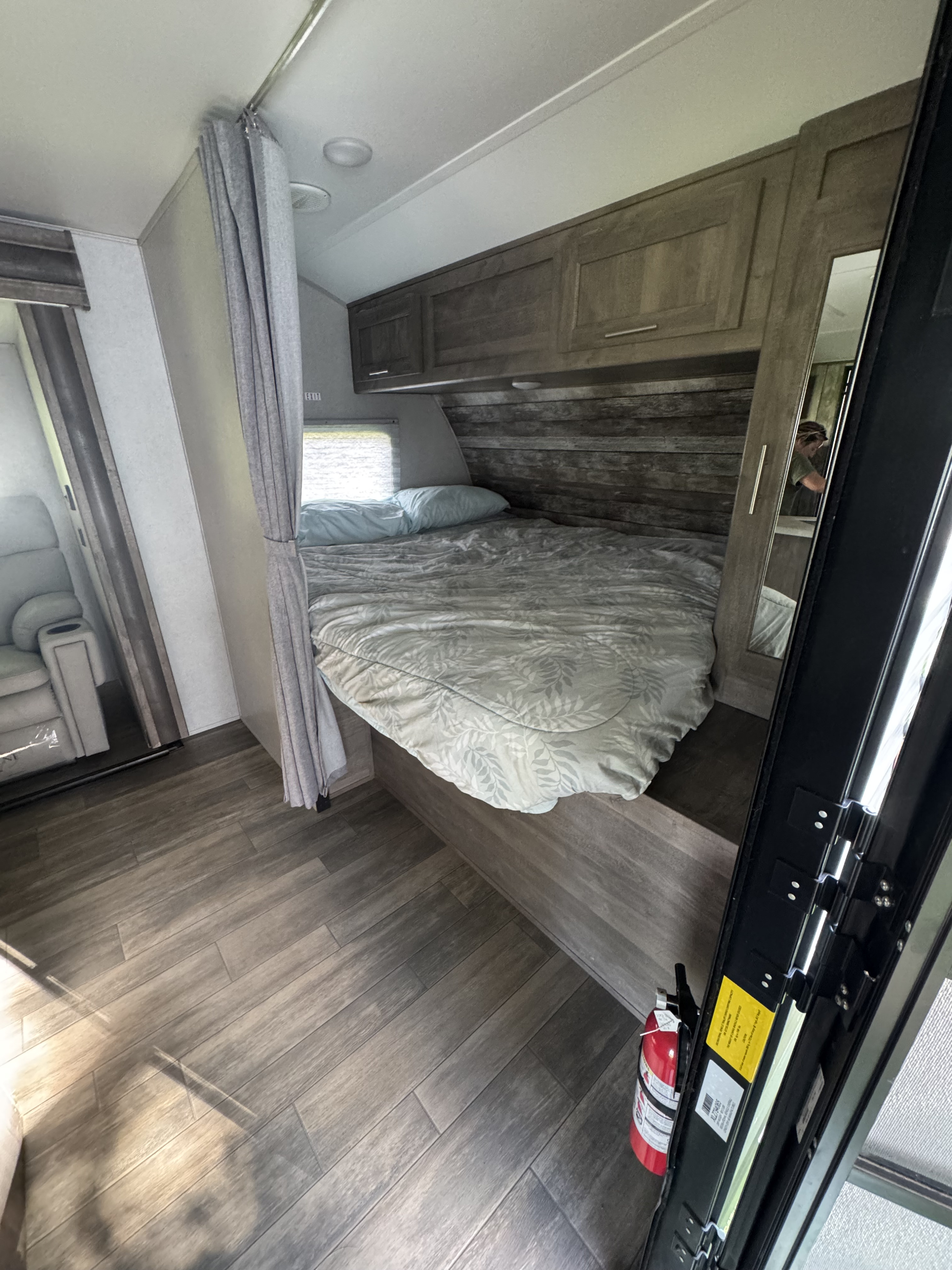 Inside this modern rv rental: a wood-accented bedroom with a comfy bed, curtains, and sleek flooring. Fire extinguisher visible.. Forest River XLR Micro Boost Toy Hauler 2022