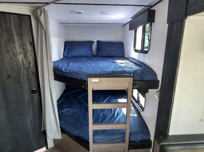 RV rental interior features two bunk beds with blue bedding and a ladder, offering compact sleeping space.. Keystone RV Hideout 2021