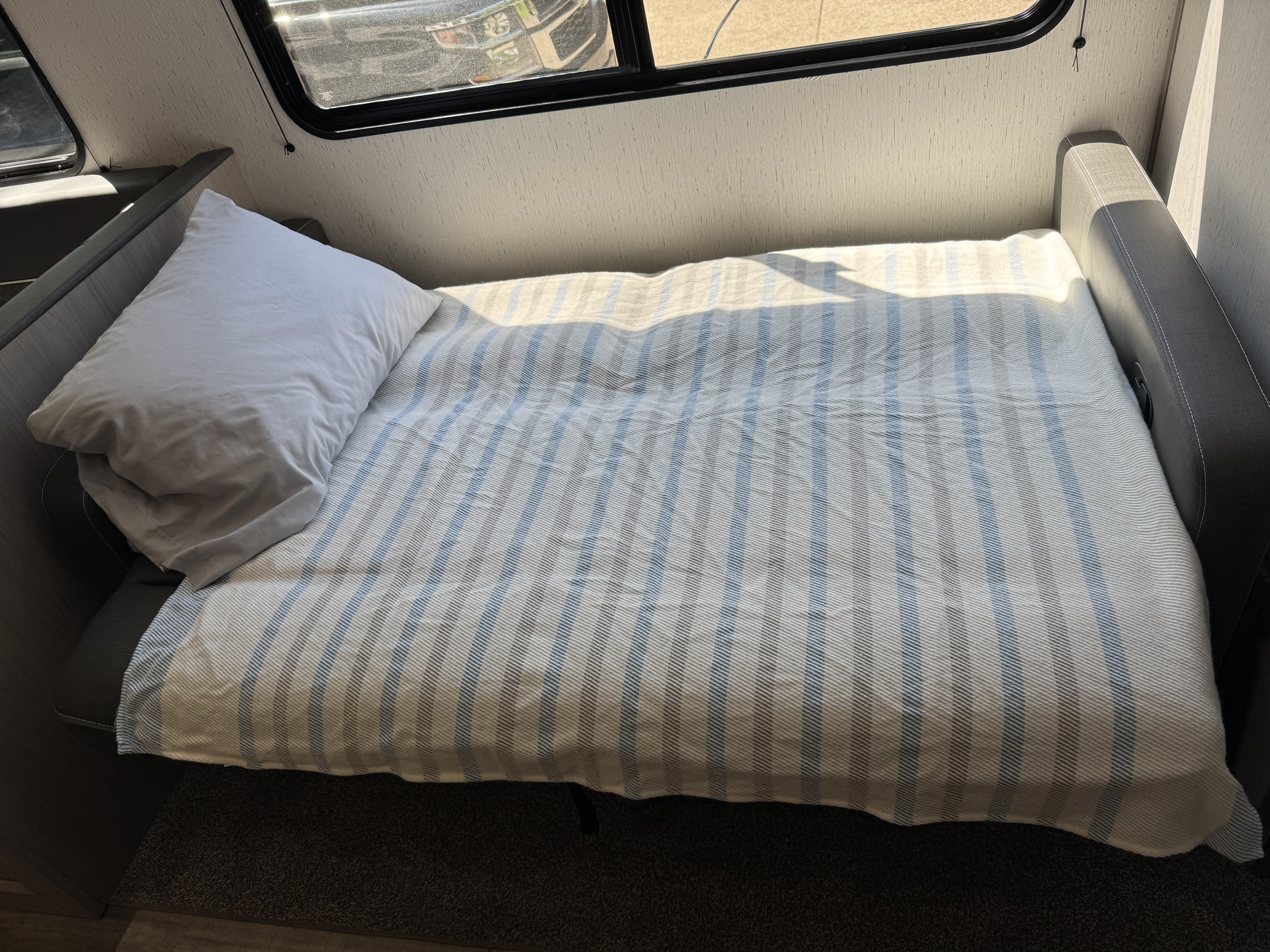 Cozy RV rental interior featuring a made-up bed with a striped blanket and pillow, bathed in bright sunlight.. Dutchmen Coleman Lantern 2022