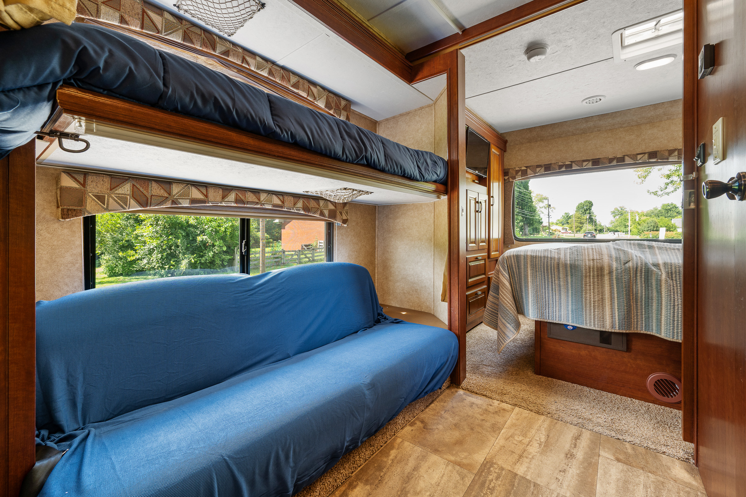 RV rental's bunk bed and blue sofa area, with a peek into the main bedroom. Scenic window view outside.. Forest River Sunseeker 2015
