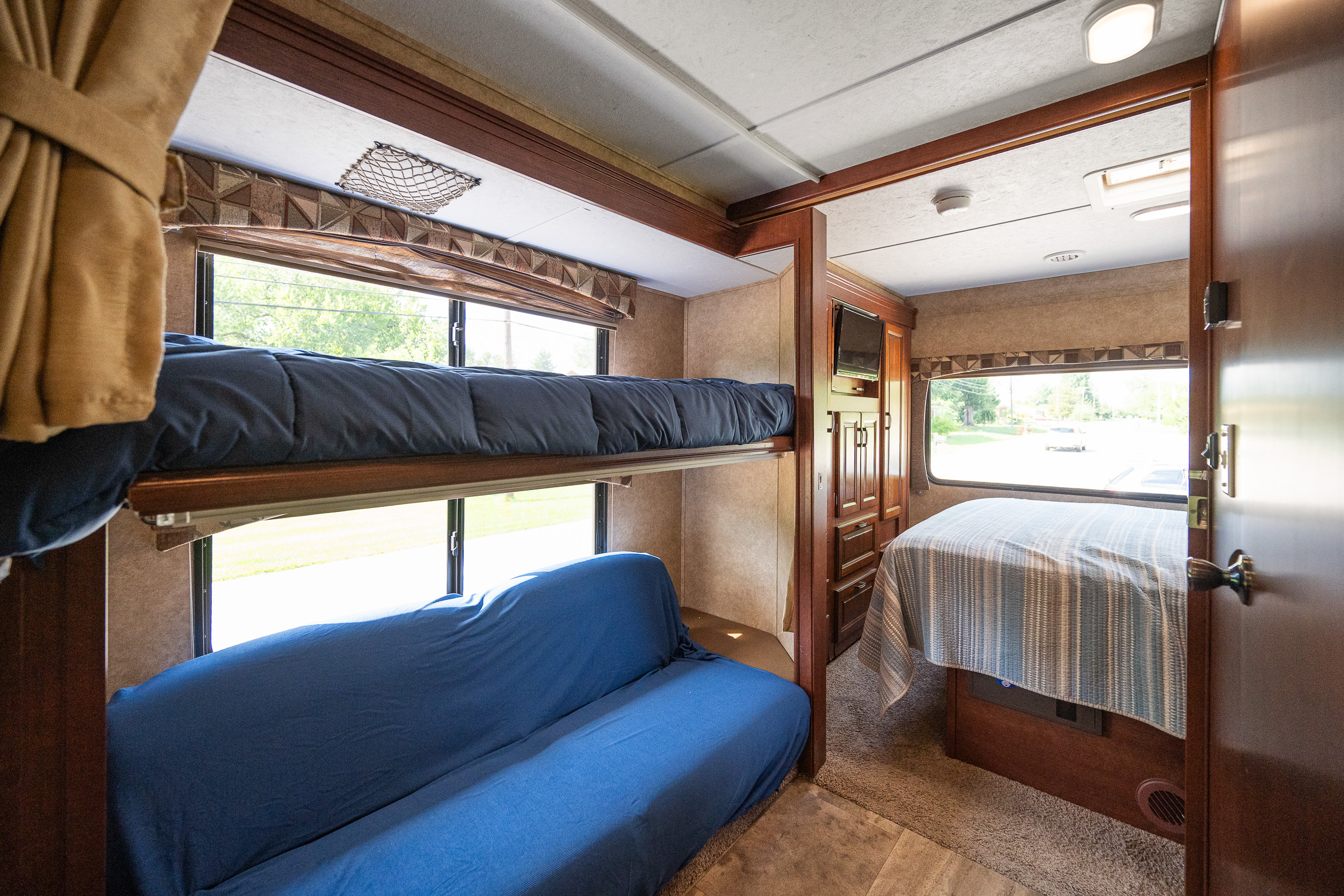 RV rental interior with bunk beds, blue couch, and a separate bedroom featuring a striped bed.. Forest River Sunseeker 2015