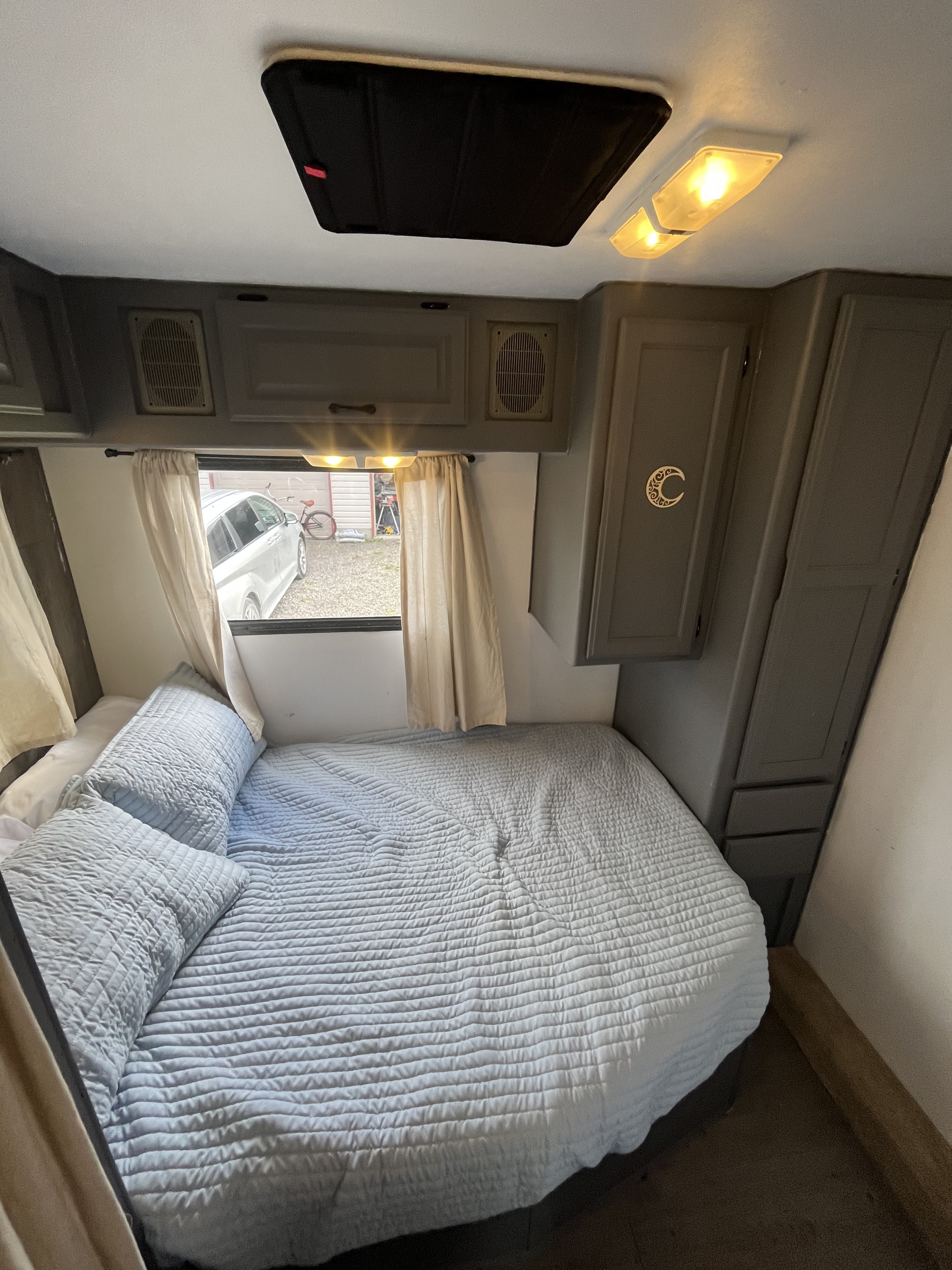 Cozy RV rental bedroom featuring a soft blue bed, window with curtains, and gray overhead cabinets.. Gulf Stream Ultra 1998