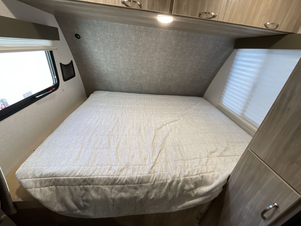 RV rental interior: A bright bedroom featuring a large bed with light bedding, dual windows, and ample overhead storage.. Minnie Micro Minnie 2022