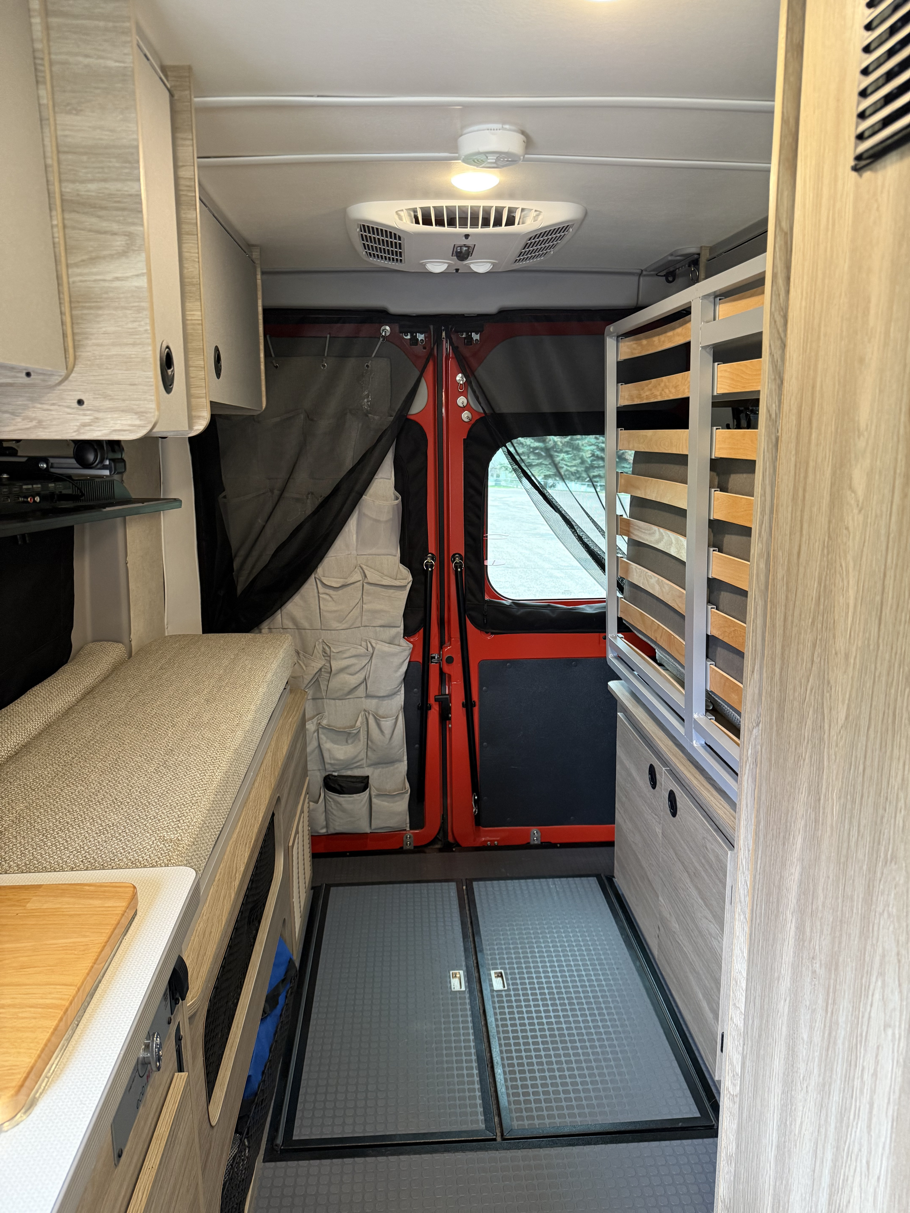 RV rental interior: rear cargo doors, compact kitchen, convertible bed/seating, and AC unit for mobile living.. Winnebago Solis 2024