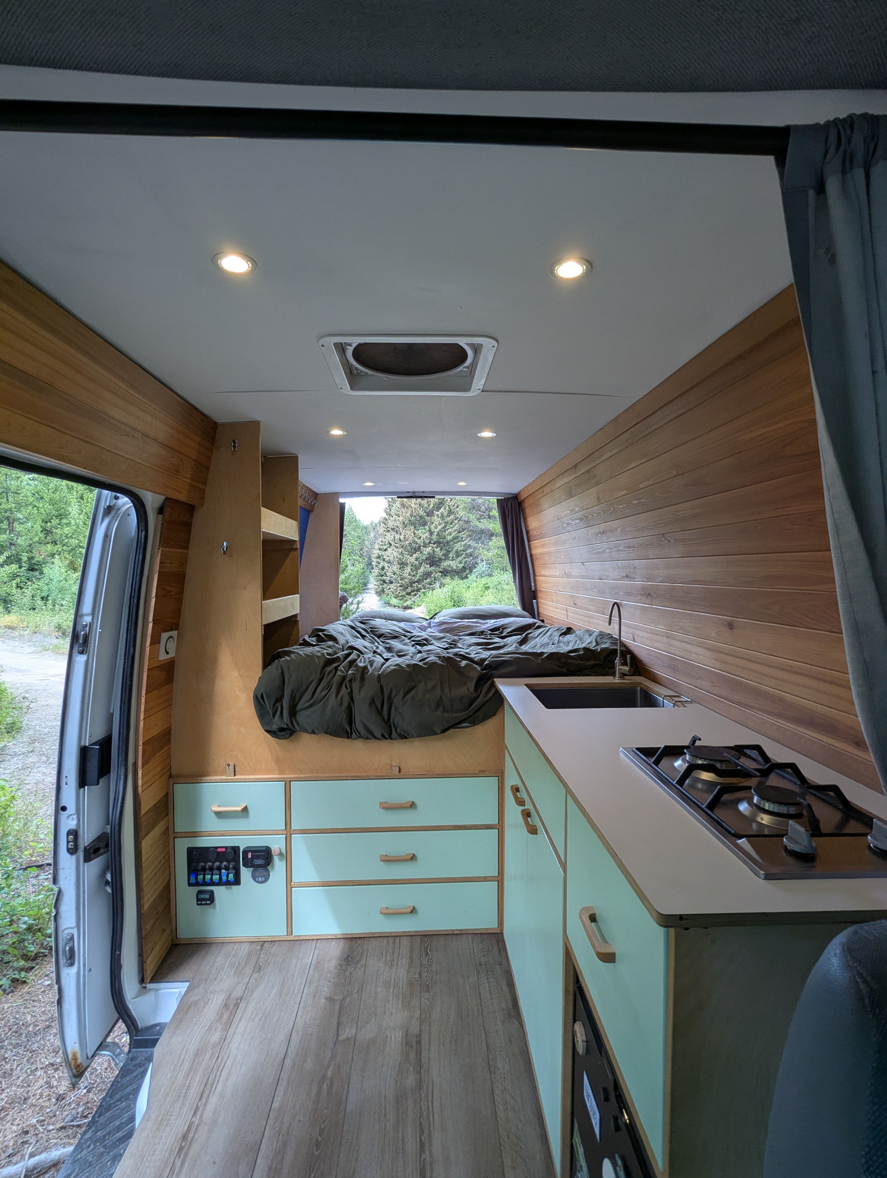 Spacious, modern RV rental interior with a cozy bed, sleek kitchen, wood paneling, and mint green cabinets, ready for adventure.. Dodge Sprinter Van 2006