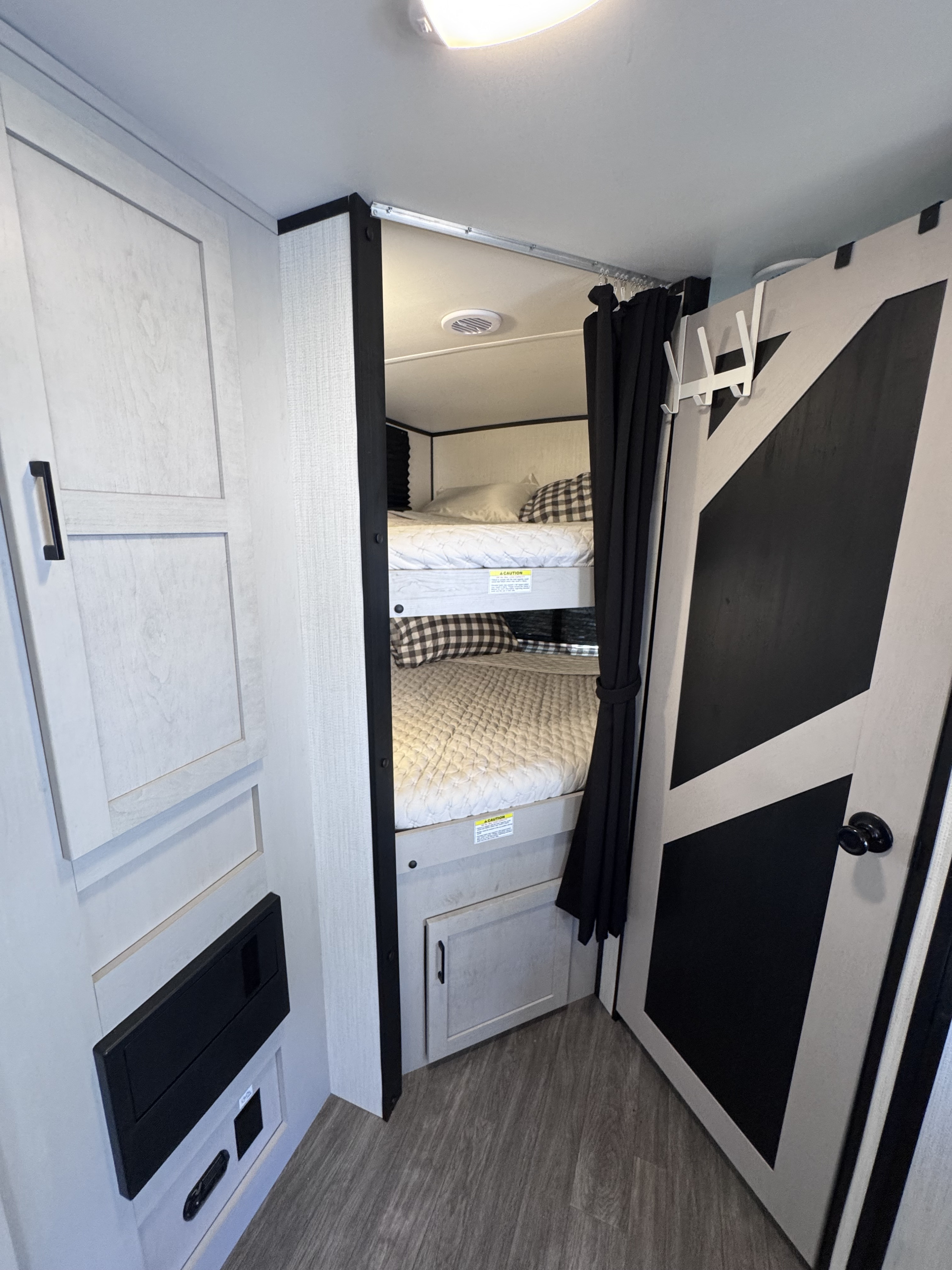 RV rental bunk beds: a cozy, modern sleeping area with black privacy curtains, checkered pillows, and light wood-grain cabinetry.. Heartland RVs Mallard 2024