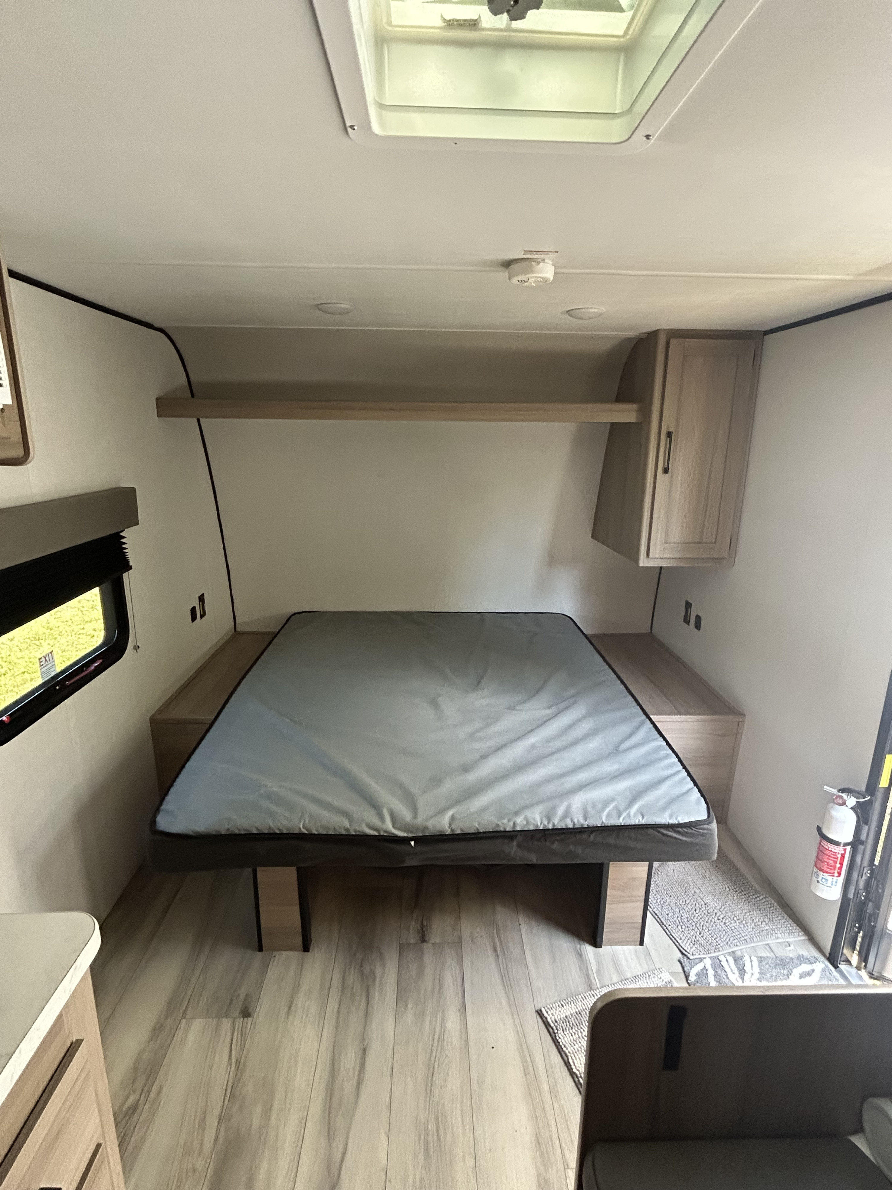 Inside an rv rental: a well-lit bedroom area featuring a neatly made bed, overhead storage, and a safety fire extinguisher.. Keystone-Coleman 17R 2025