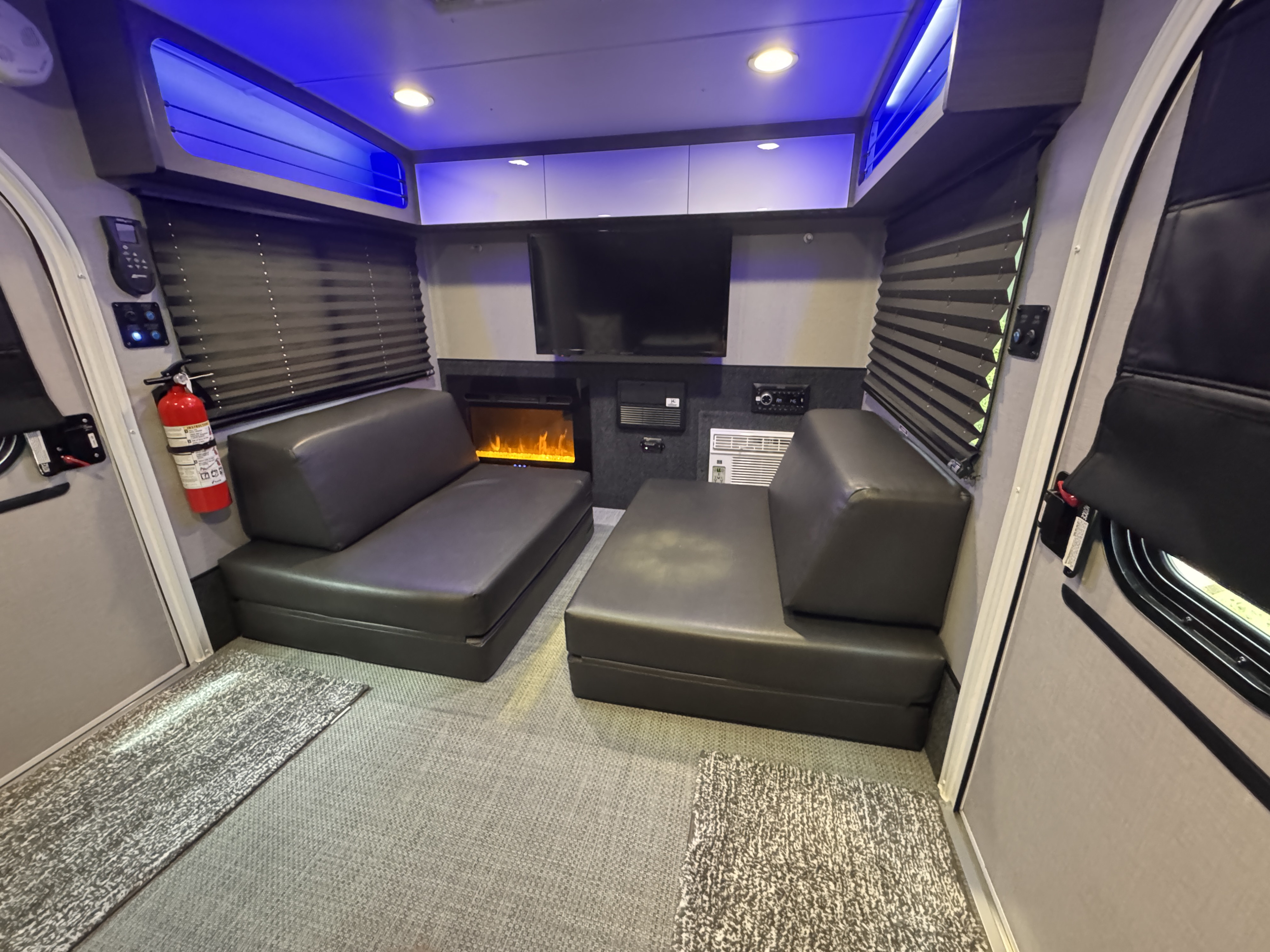 Modern rv rental interior with black convertible sofas, TV, fireplace, and blue ambient lighting for relaxing travels.. InTech RV Luna 2022