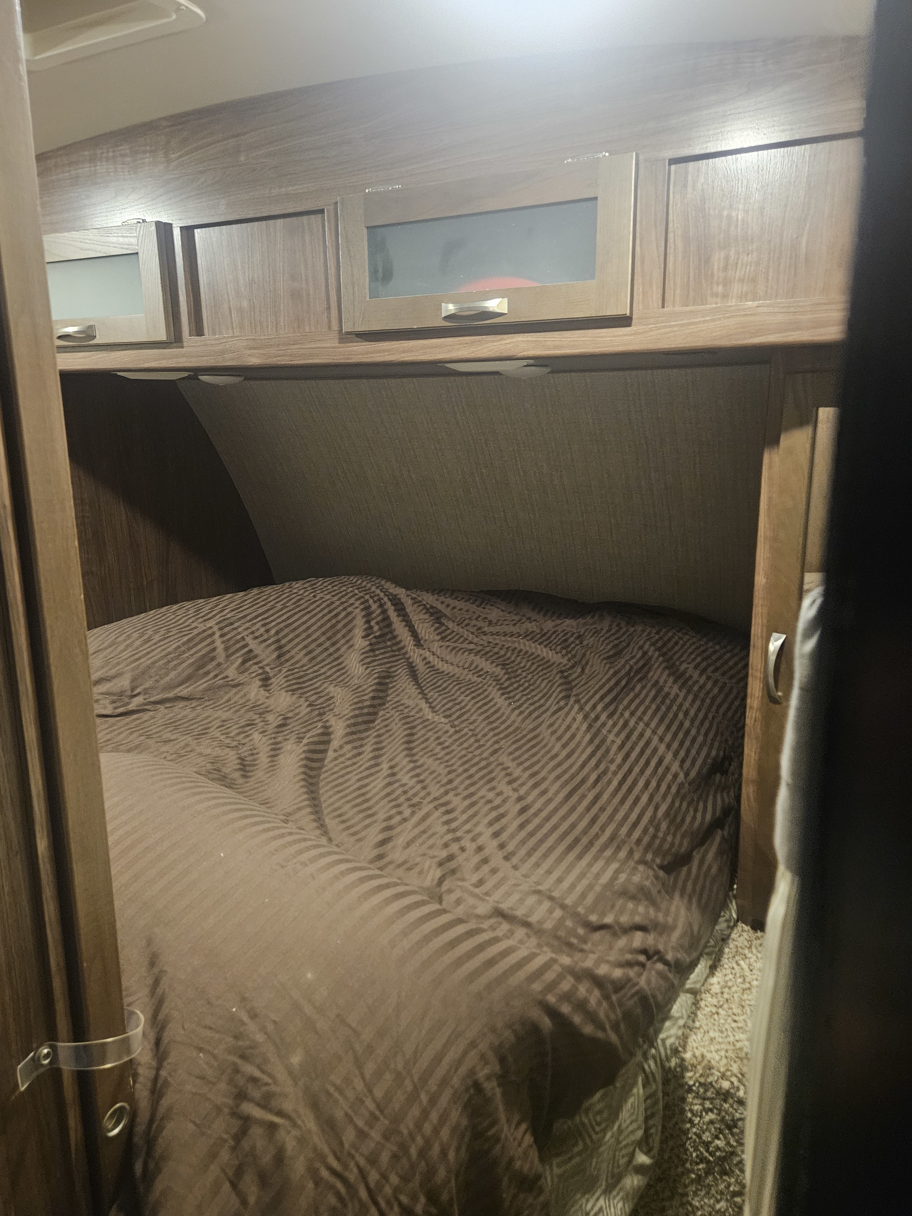 Cozy RV rental bedroom featuring a striped bed and overhead cabinets, providing a comfortable sleeping space.. Dutchmen 242bhsl 2017