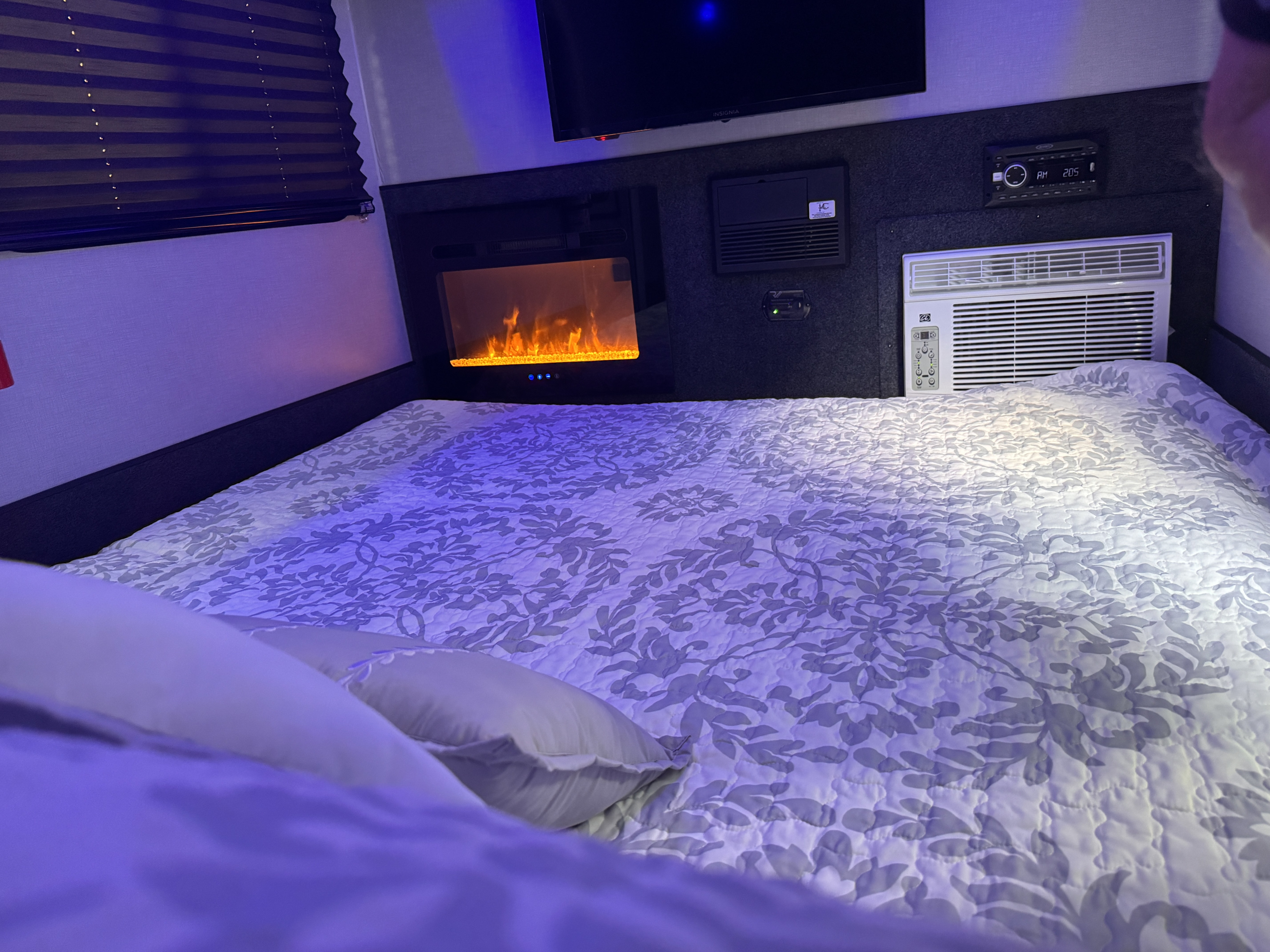 Experience comfort in this RV rental bedroom with a cozy bed, electric fireplace, TV, and AC unit.. InTech RV Luna 2022
