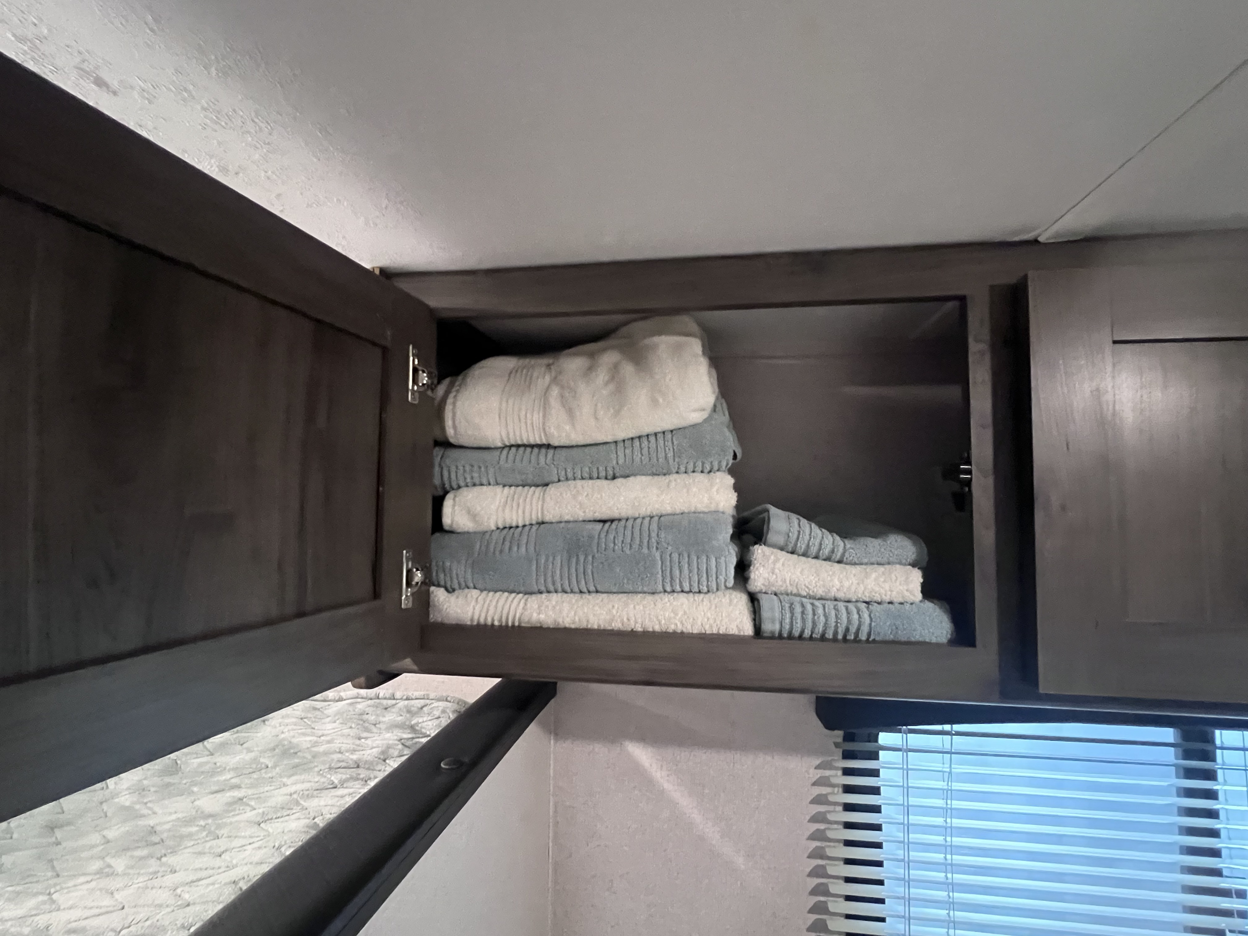 RV rental bedroom storage: Neatly folded white and blue towels in an open overhead cabinet, a typical RV interior.. Coachmen Viking Saga 17BH 2021