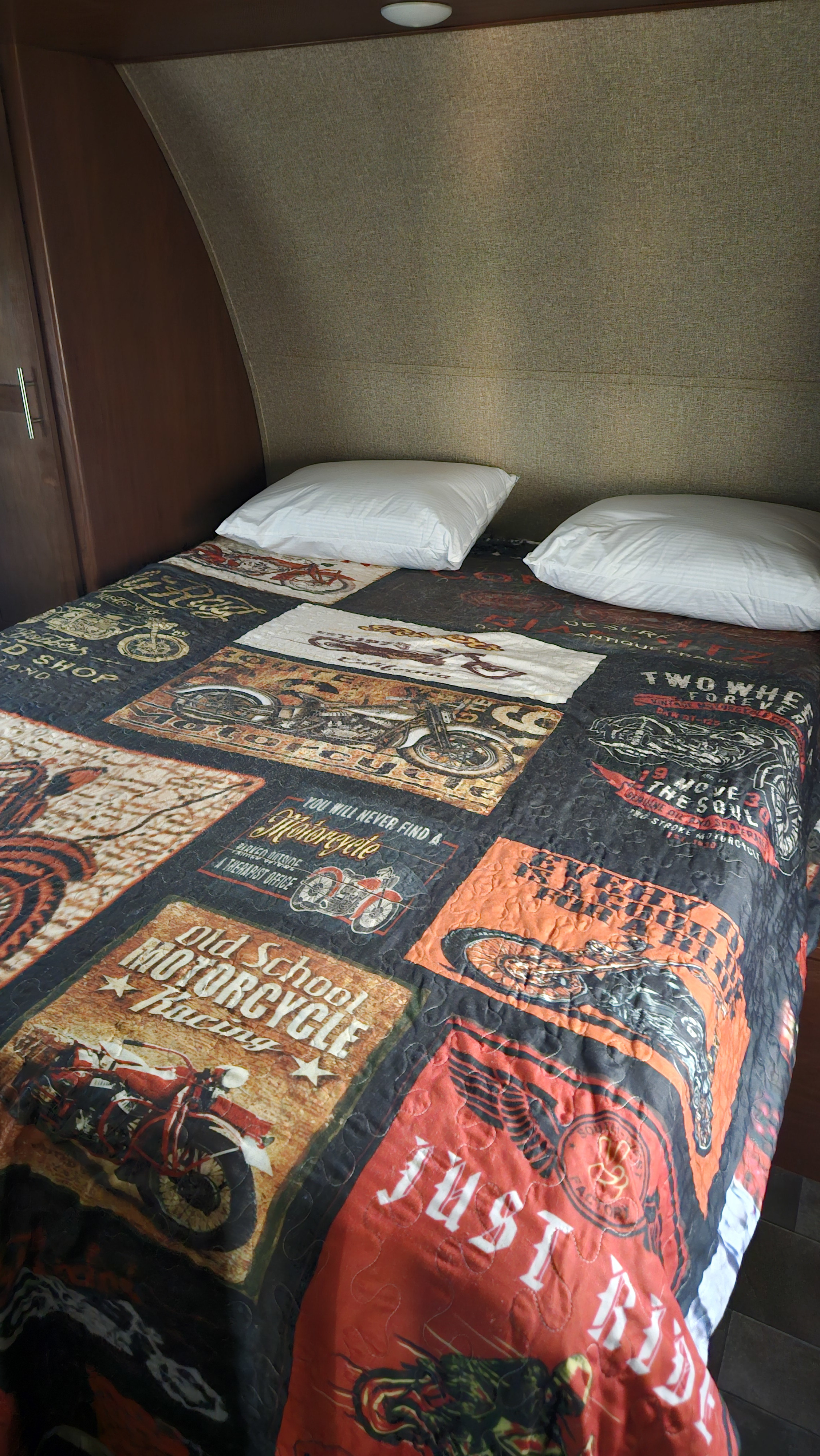 RV rental bedroom: A comfortable bed featuring a unique motorcycle-themed quilt and two white pillows.. Forest River Vengeance Toy Hauler 2016