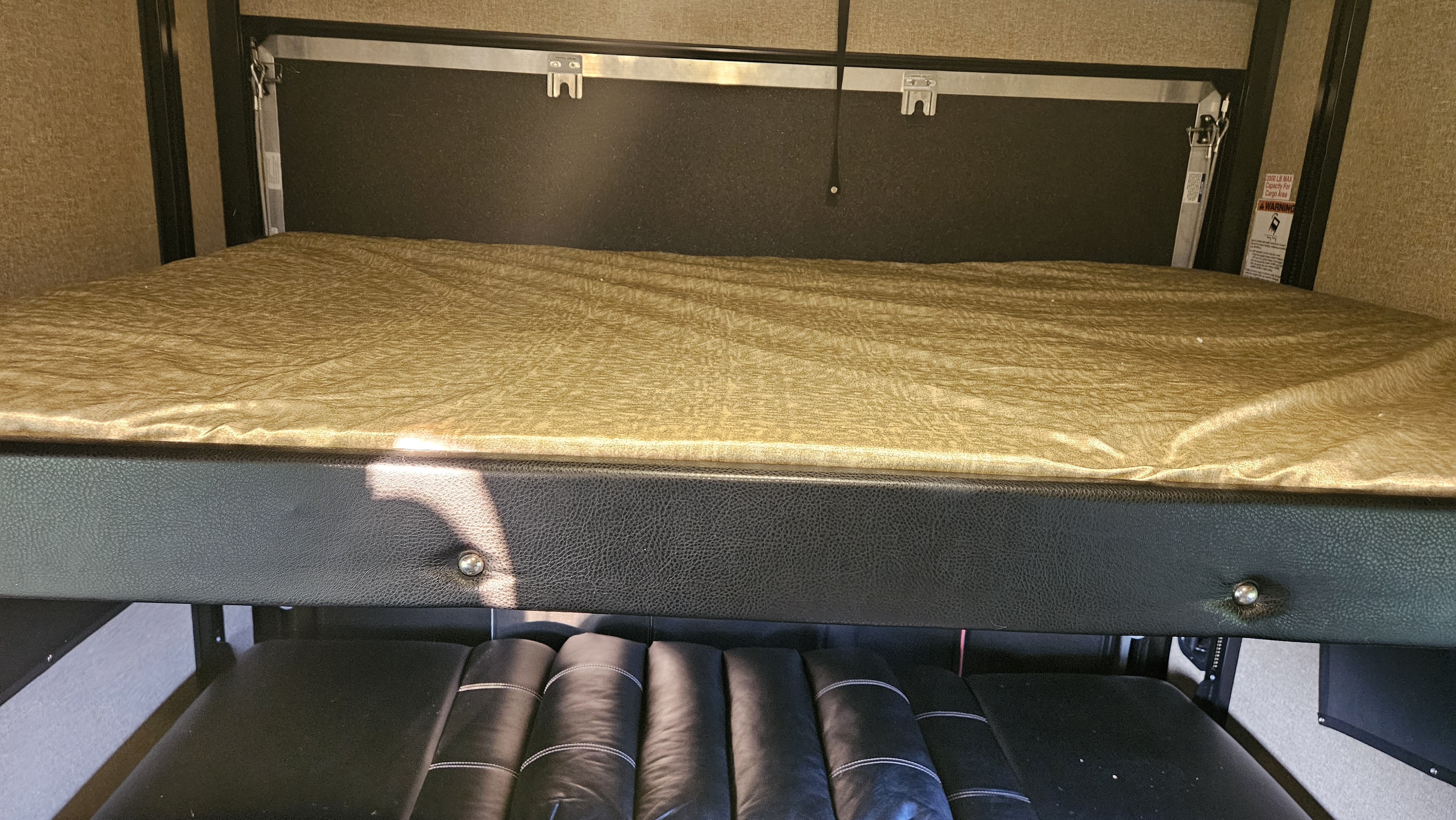 An RV rental interior: a raised bunk bed with a gold mattress sits above a black upholstered couch, optimizing space.. Forest River Vengeance Toy Hauler 2016
