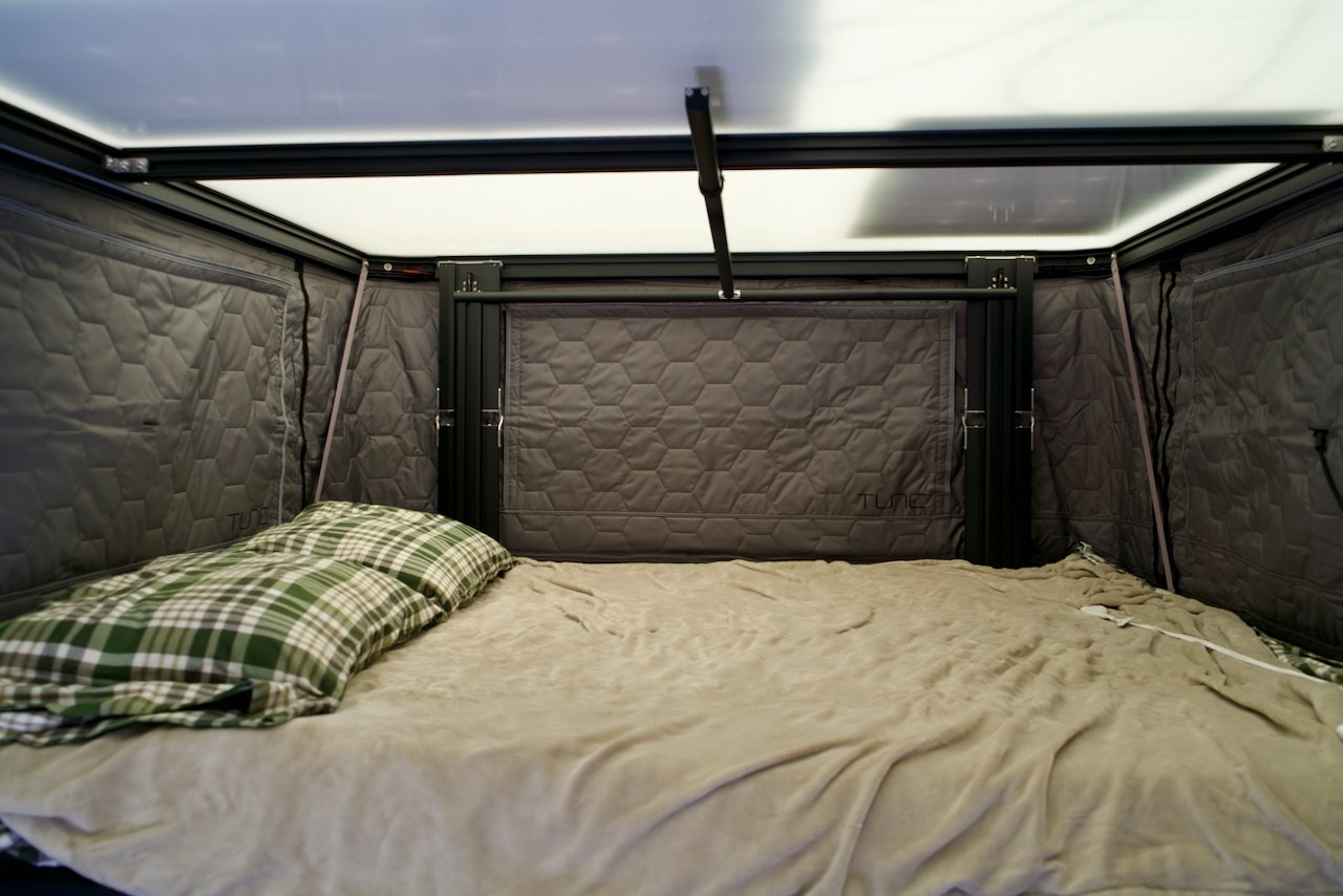 Inside a cozy RV rental: a compact sleeping area with quilted walls, a comfy bed with a plaid pillow, and overhead translucent panels.. Ford Ranger 2300 Cc 2021