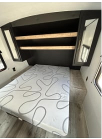 Experience RV rental comfort! This bedroom features a patterned mattress, wooden shelves, and mirrored cabinets above the bed.. Keystone RV Springdale 2022
