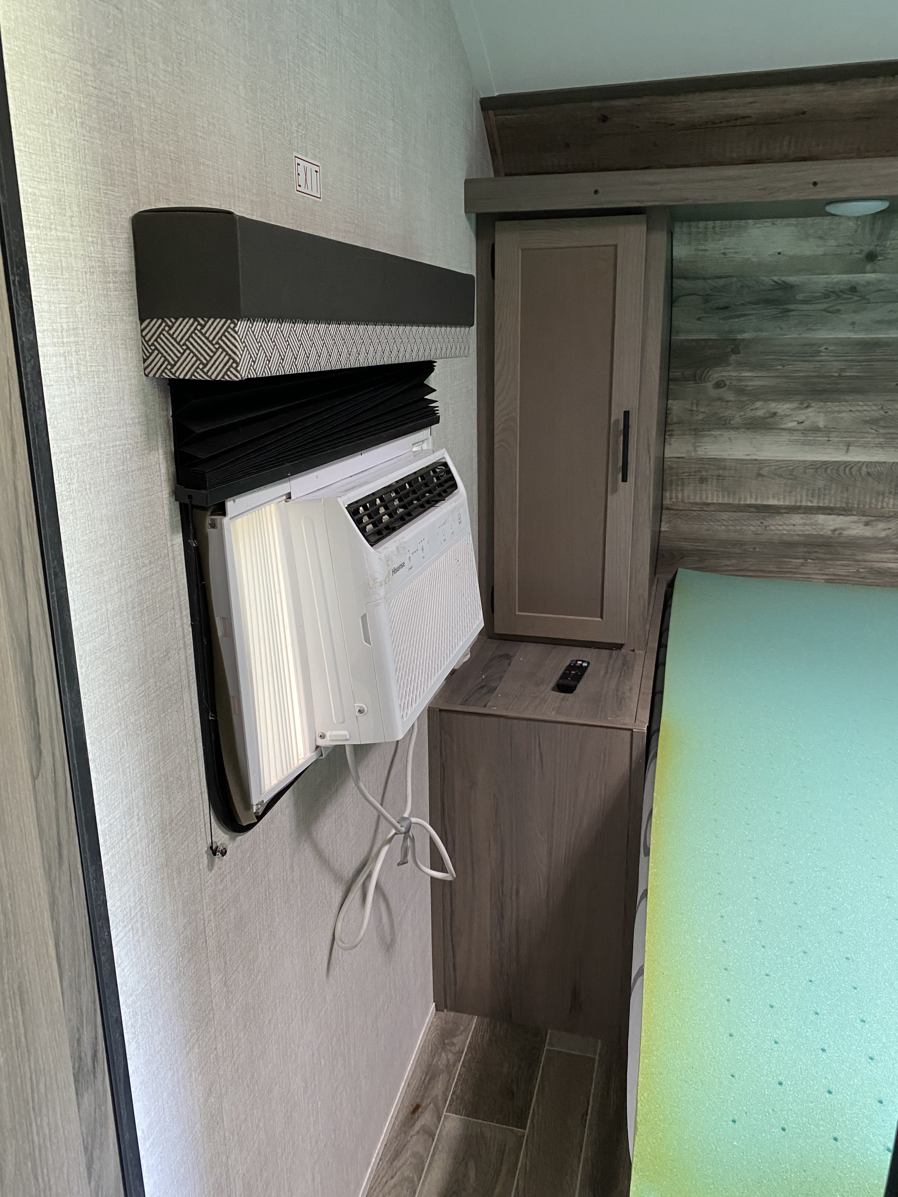 RV rental: Compact bedroom with a thru-wall AC unit partially pulled out, a cabinet, bed with green mattress, and EXIT sign.. Gulf Stream Kingsport Super Lite 2022